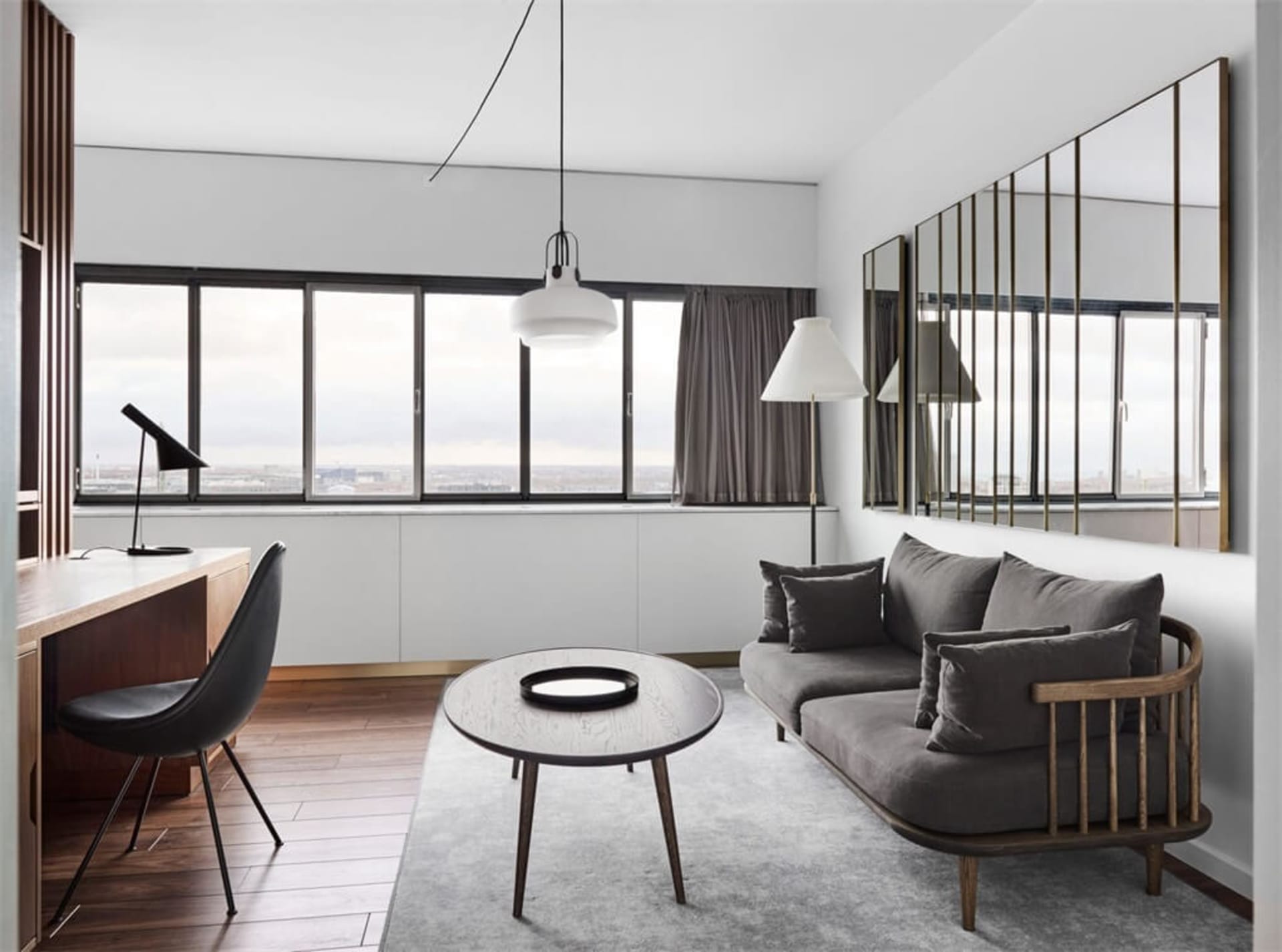A minimalist living room with a grey sofa, wooden coffee table, and a large window.
