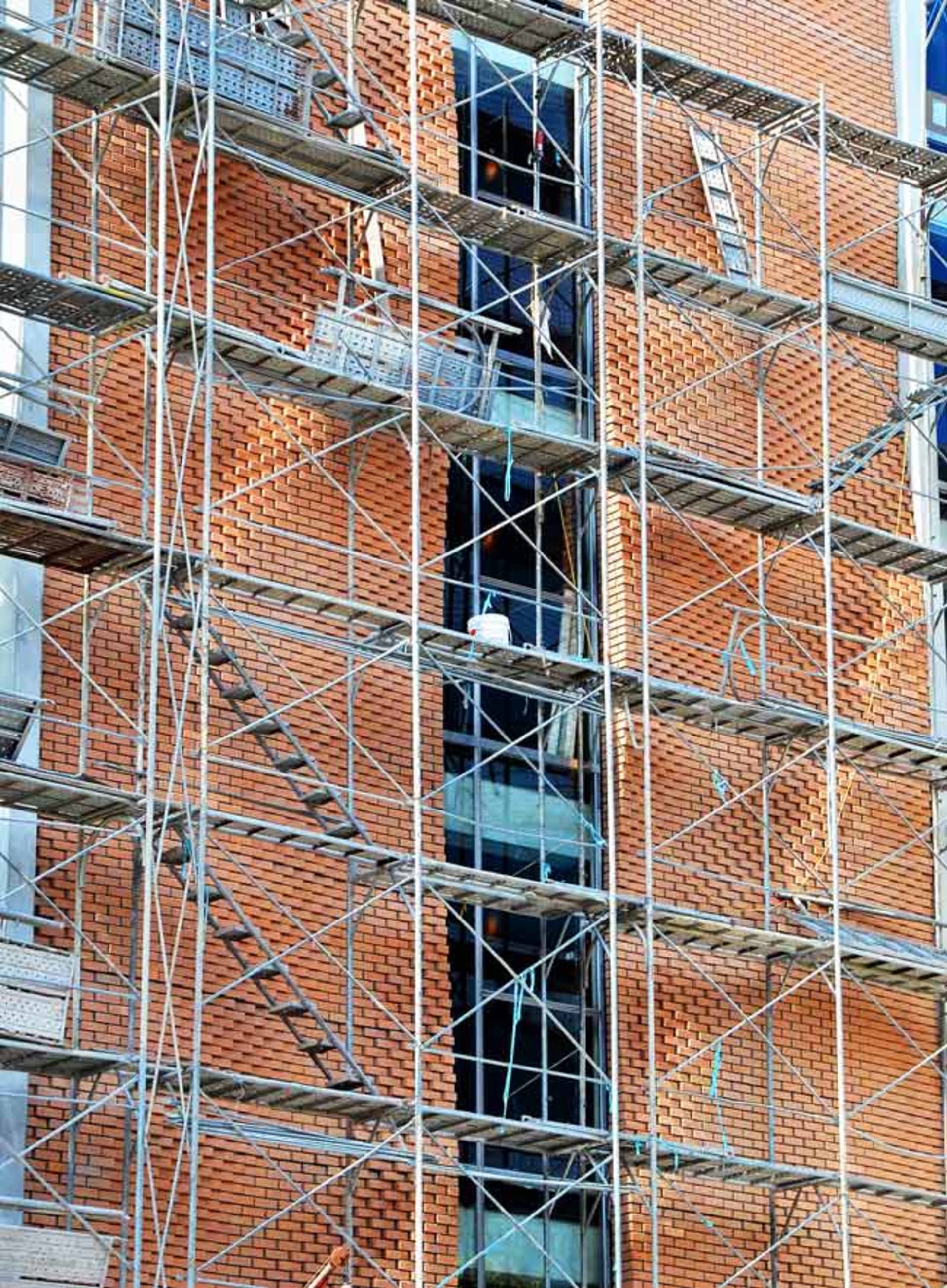 Steel scaffolding frames surrounding an unfinished brick building under construction.