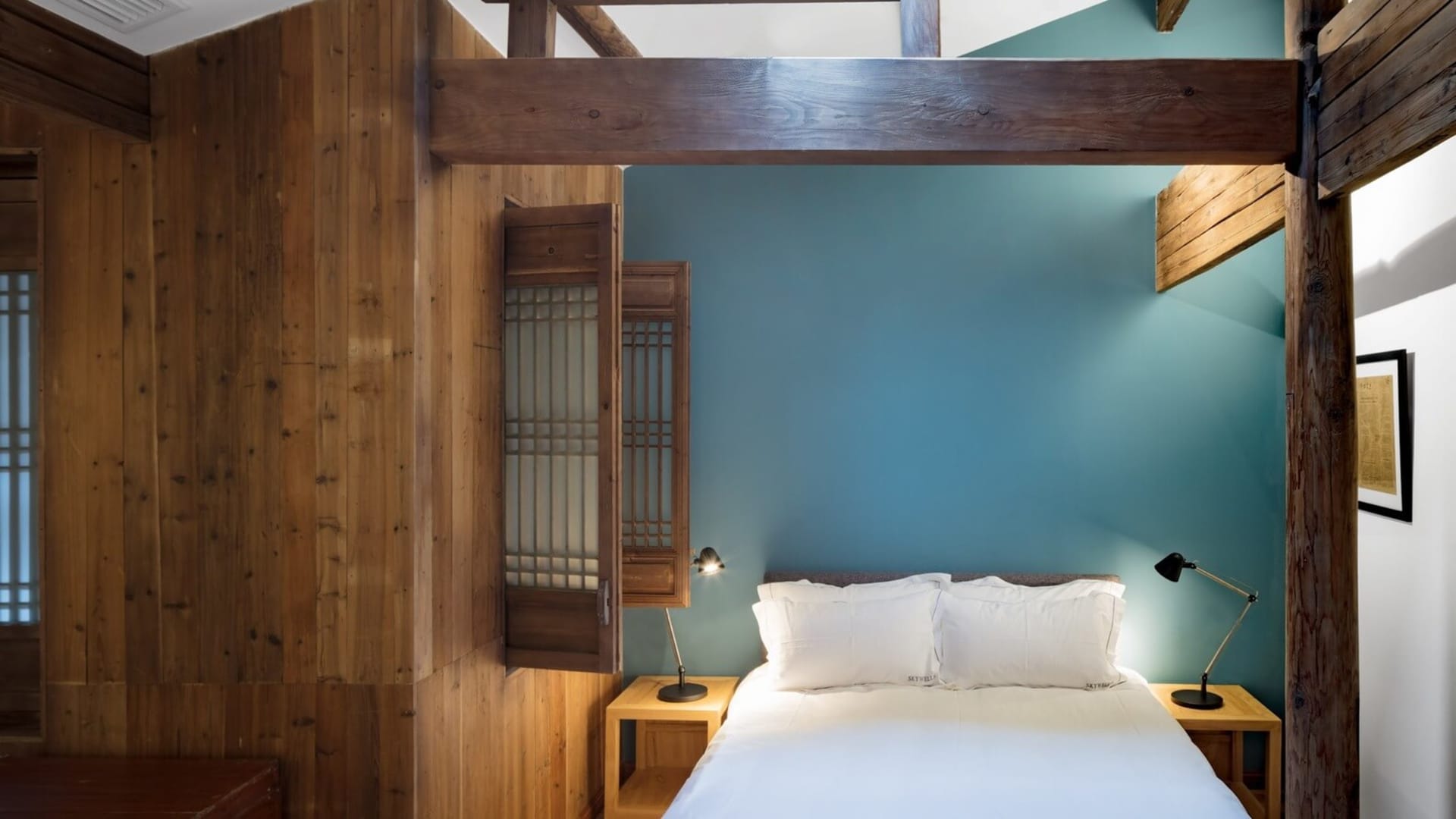 A minimalist bedroom with blue walls and wooden furniture, featuring a comfortable bed with white bedding and two bedside tab