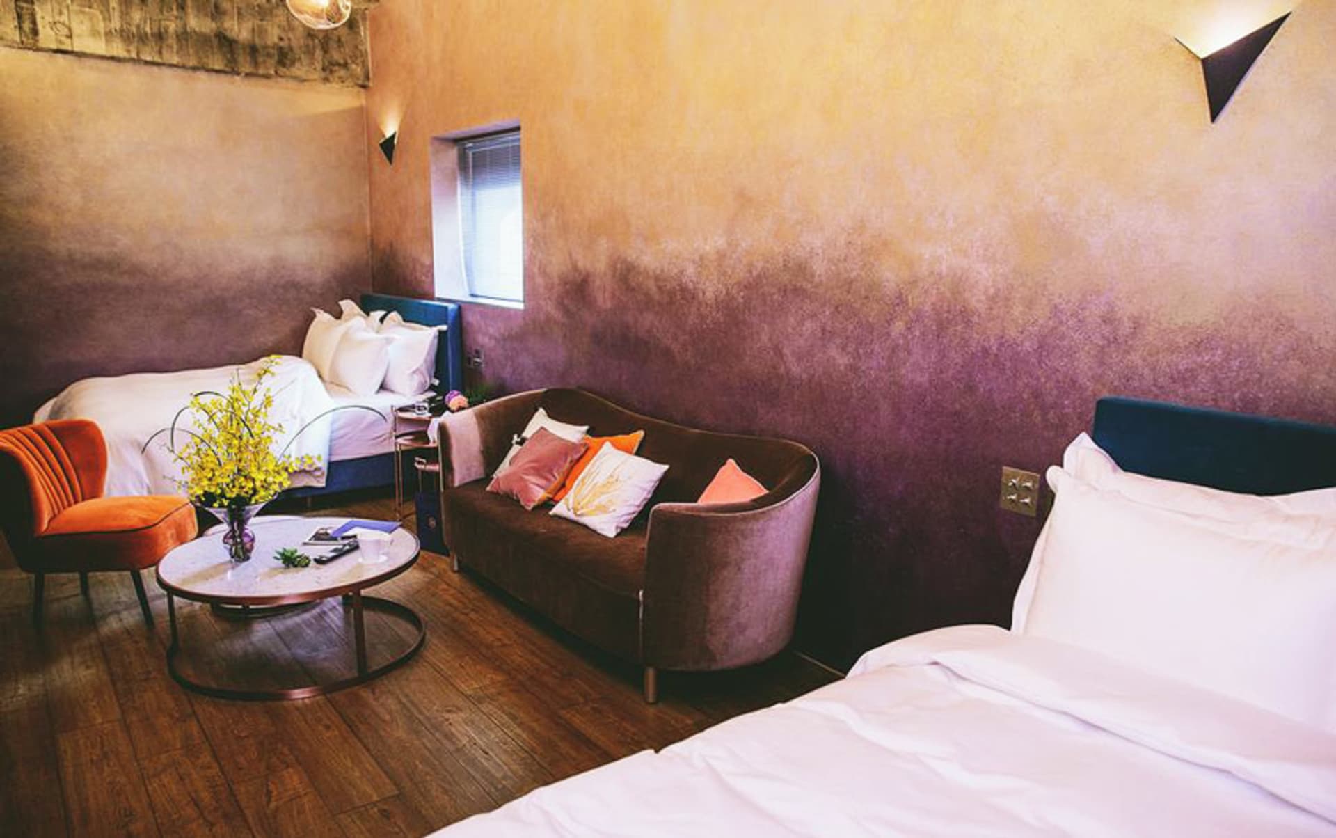 A minimalist bedroom with a velvet couch, wooden flooring, and plaster walls.