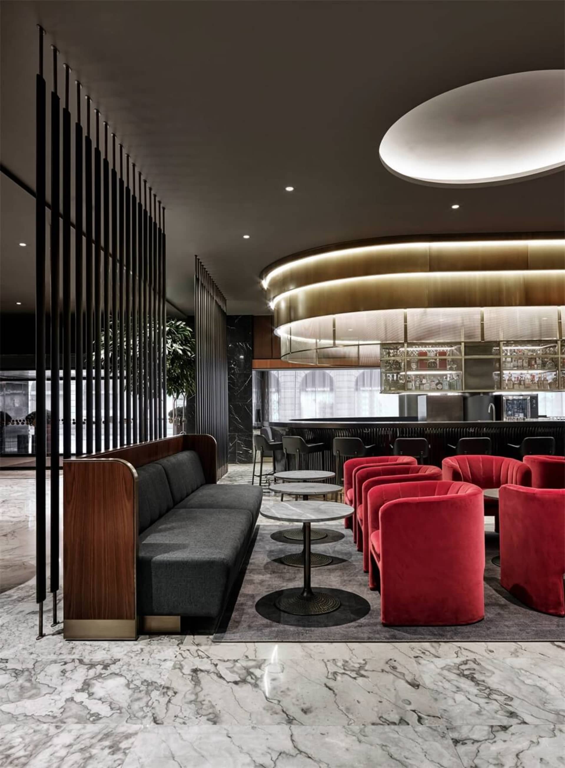 Modern coffee shop interior featuring marble floors, metallic railings, and red velvet seating.