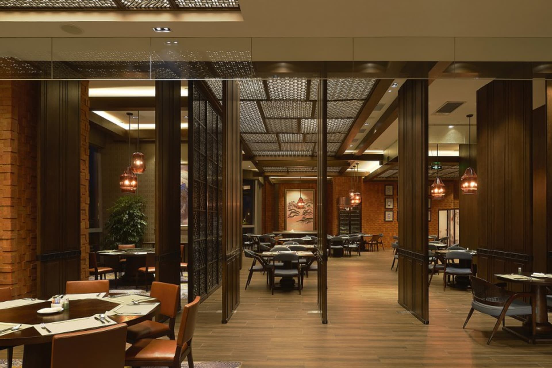 A contemporary restaurant interior with wooden tables, brick walls, and glass pendant lights hanging above round tables.