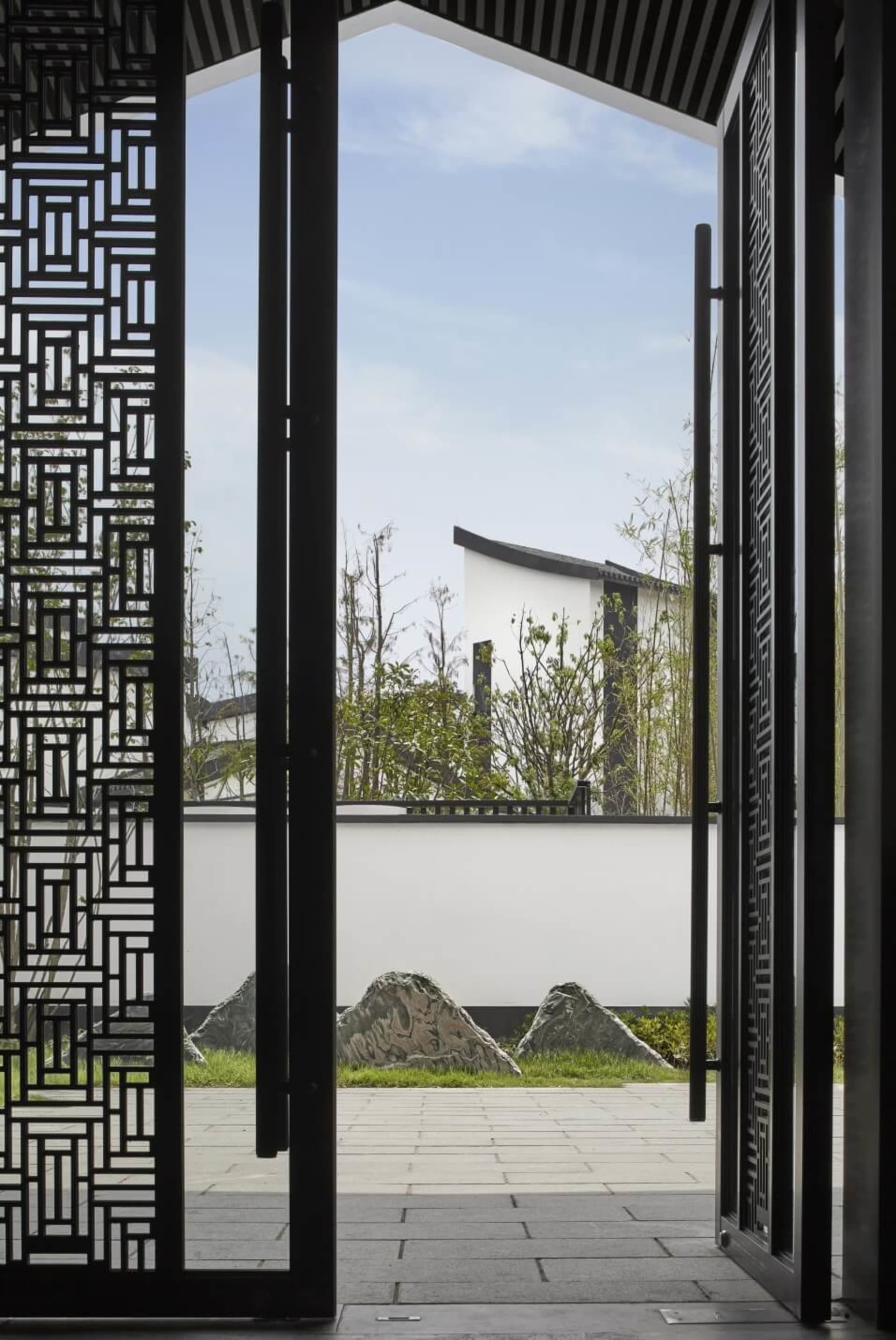 Modern garden featuring a glass wall with intricate patterns, set against a serene outdoor backdrop with greenery and stone a