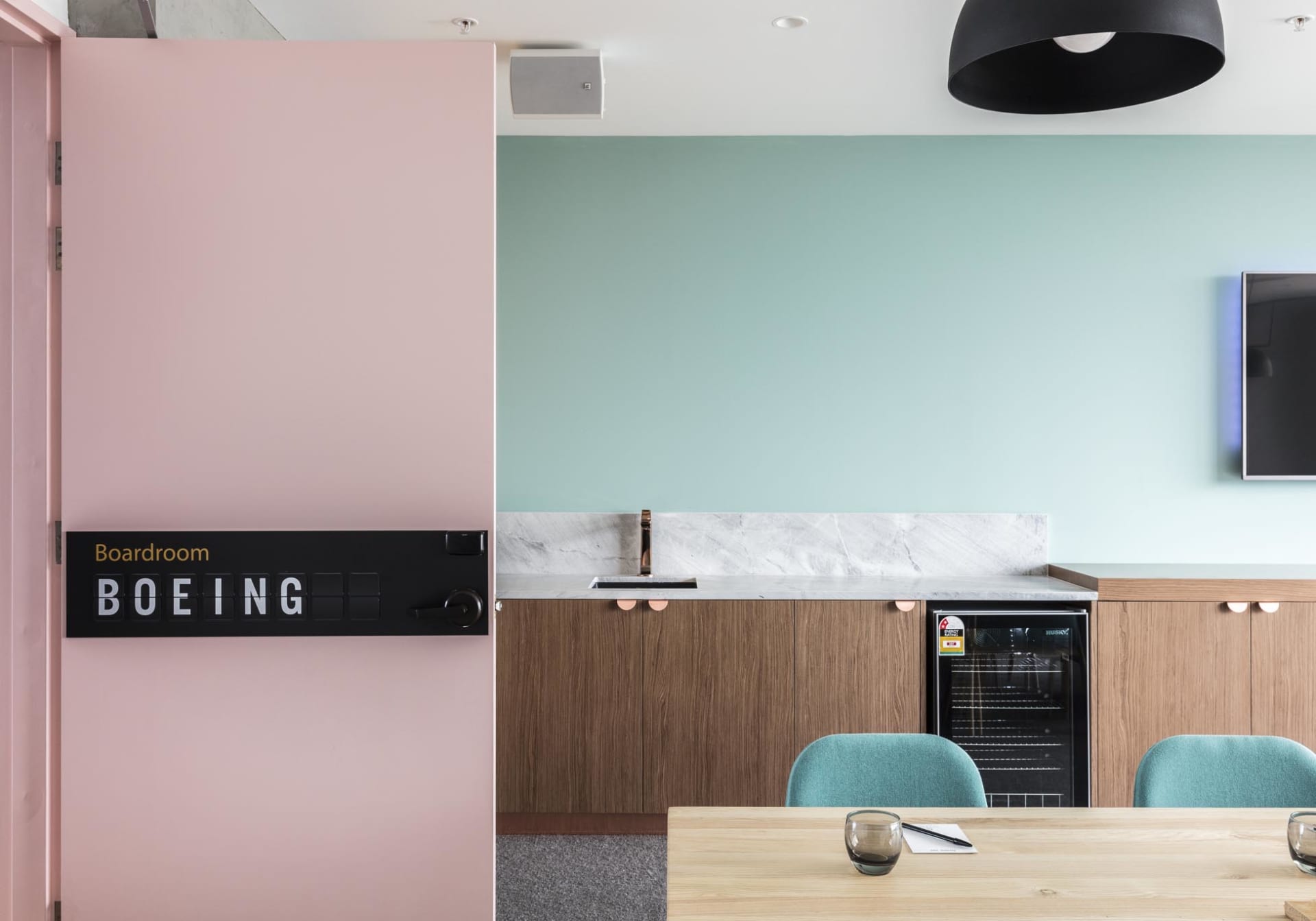 A modern office space featuring an industrial design with pink and green walls, wooden tables, and a kitchenette area.
