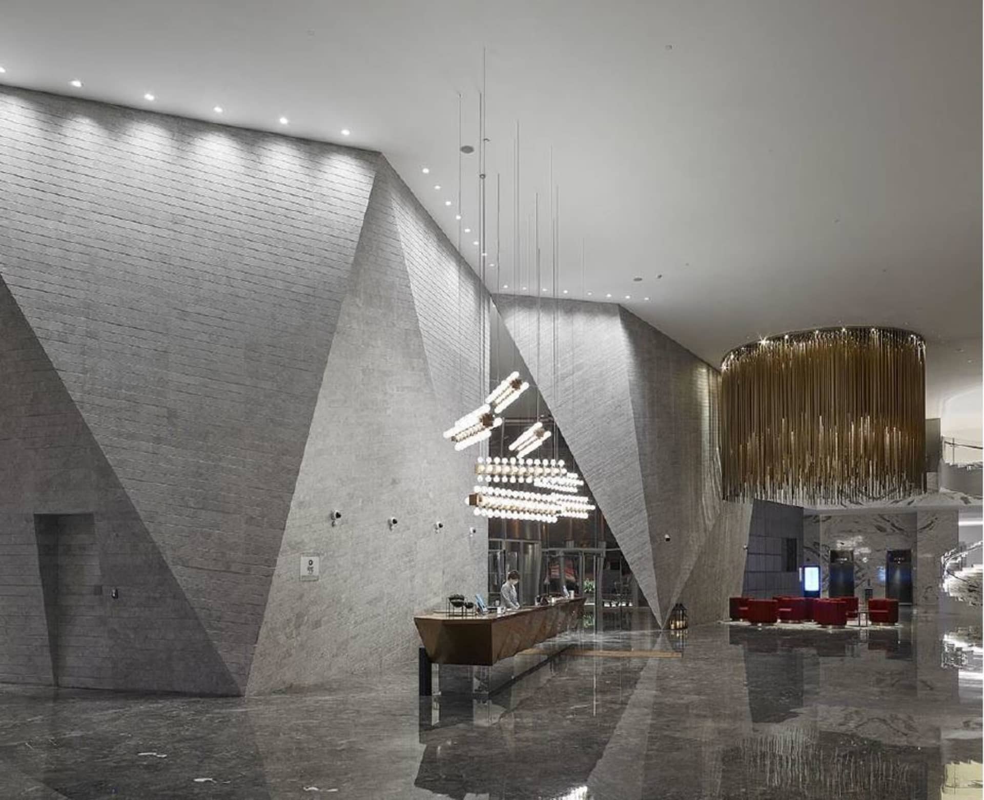 A modern lobby with concrete walls and ceiling, geometric lighting fixtures, and a reception desk.