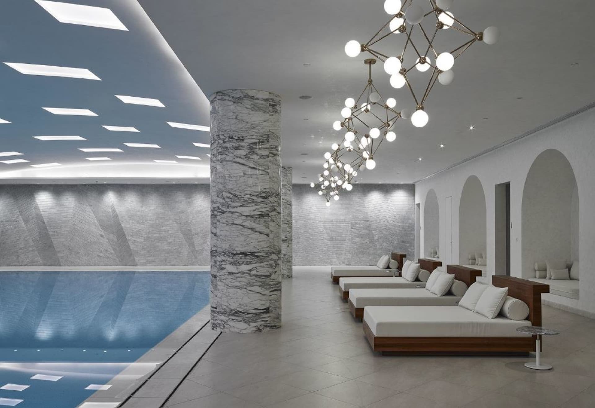 A modern spa relaxation room featuring marble columns, concrete walls, and wooden lounge beds.