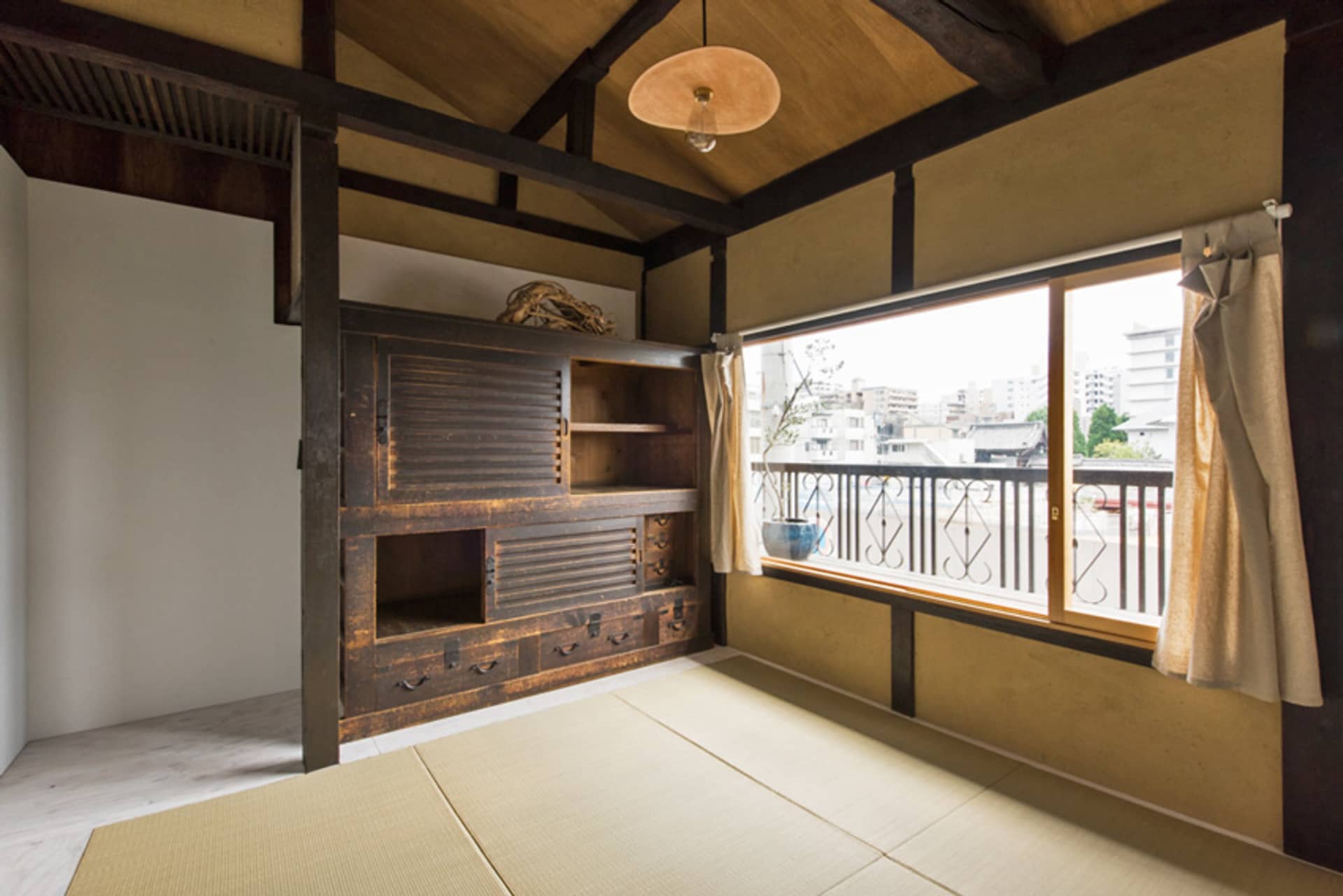 Traditional Japanese room with wooden shelves, tatami mats, and a view of the city through a large window.