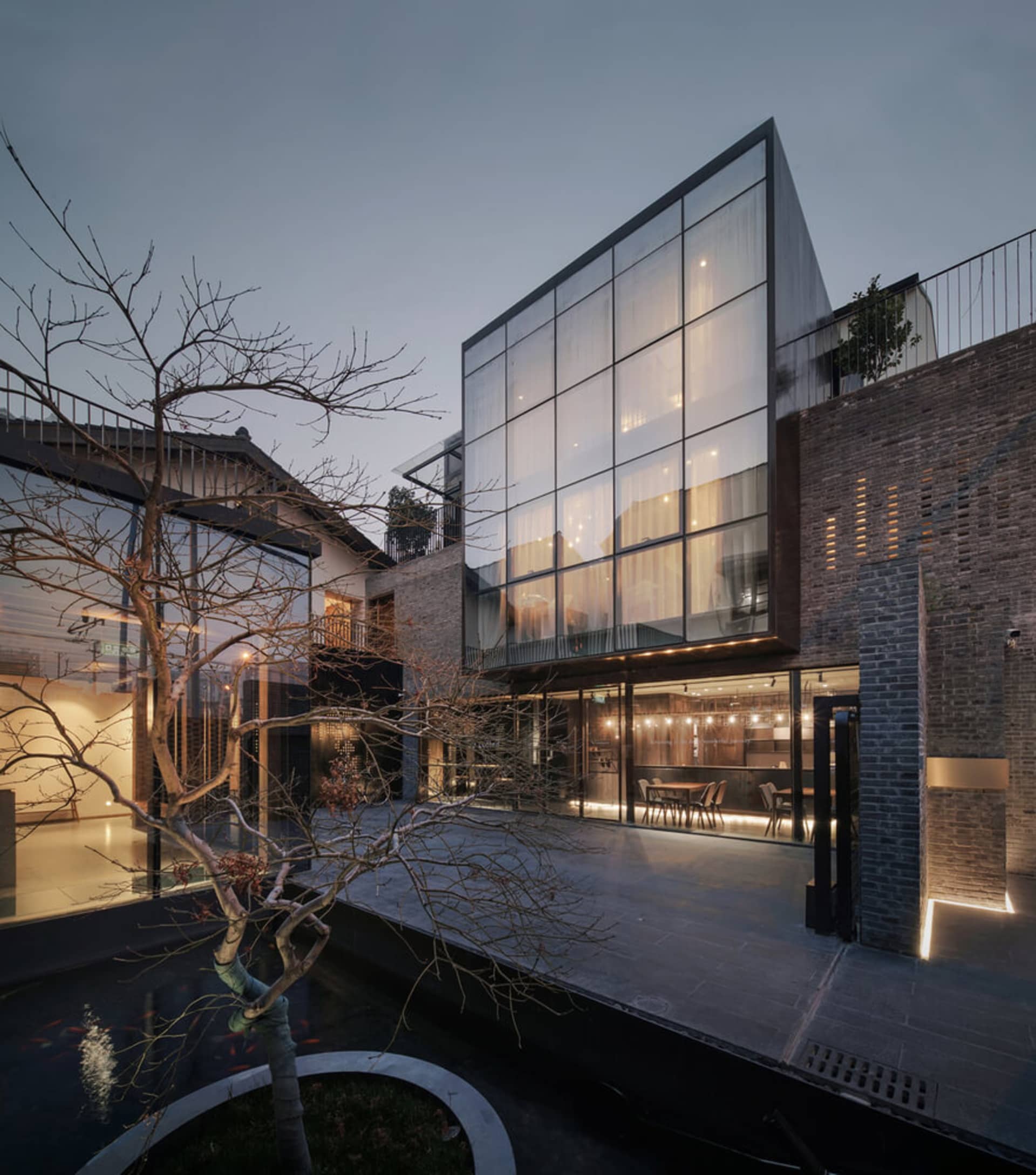一棟現代住宅建築，擁有大型玻璃窗與磚牆，內部舒適空間散發溫暖燈光。