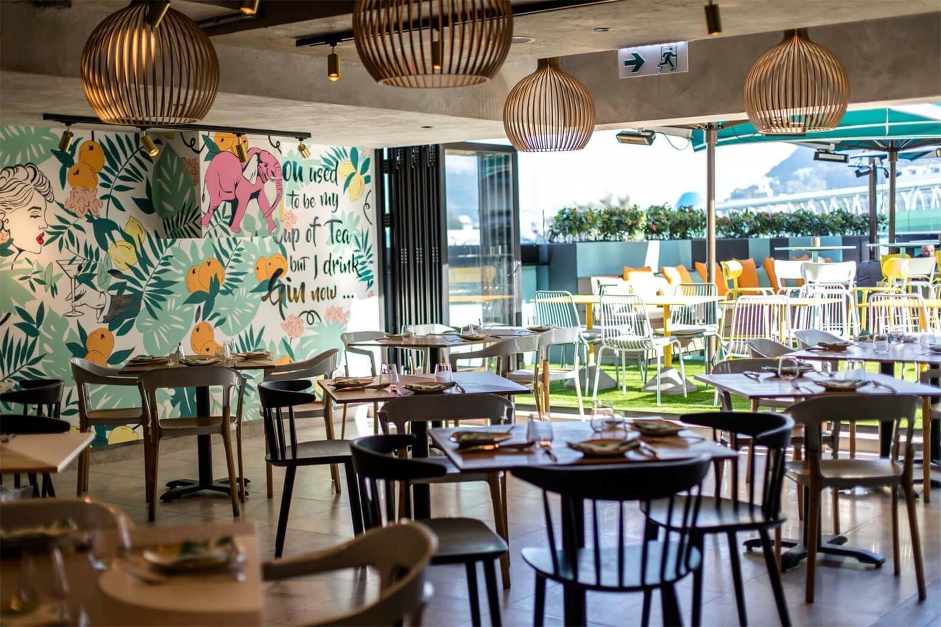 Modern bar and cafe with indoor plants and hanging light fixtures.