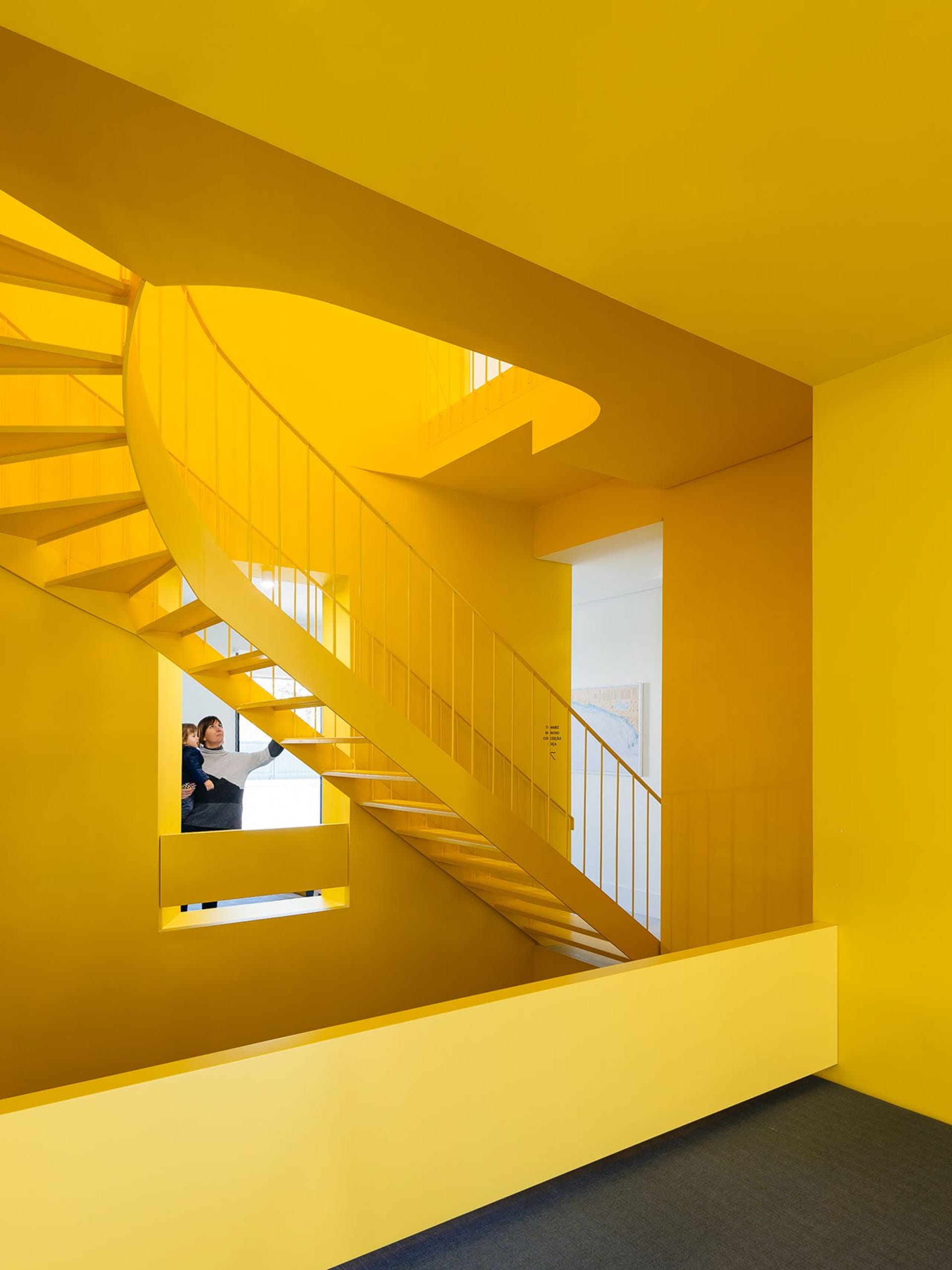A modern, brightly colored yellow spiral staircase with a person and child looking up.