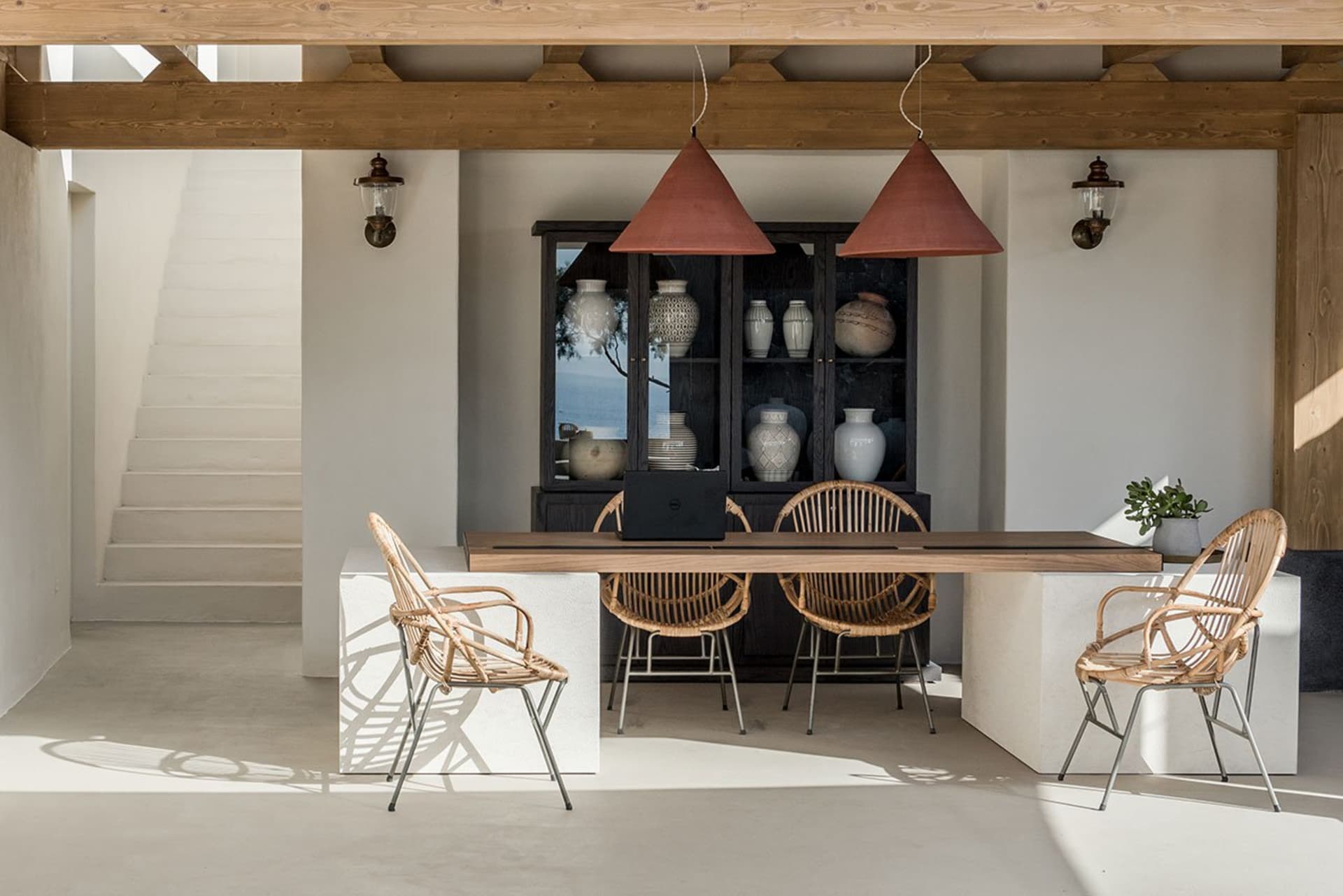 Modern minimalist dining room featuring concrete flooring, rattan chairs, and a wooden dining table.
