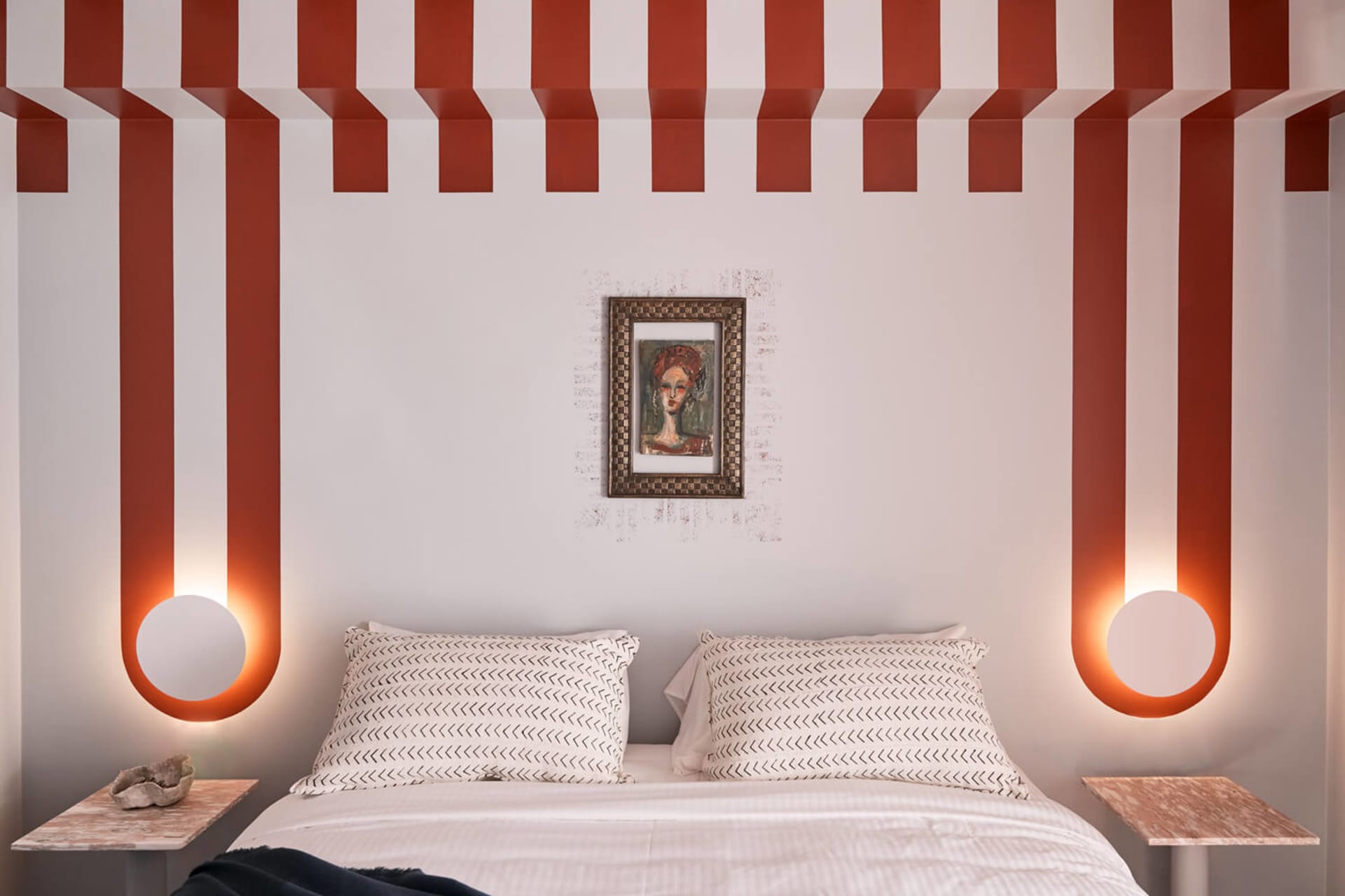 A modern bedroom with a striped ceiling, patterned bedding, and a framed abstract portrait on the wall.