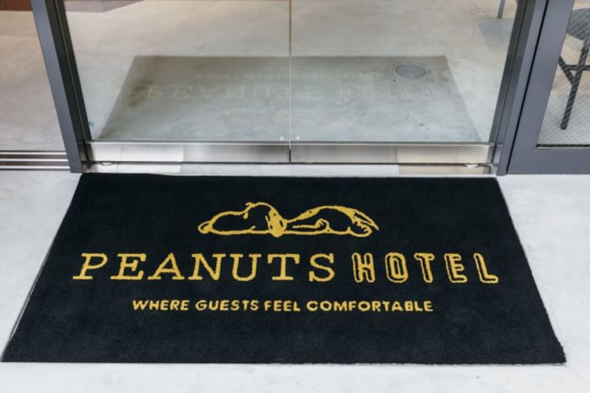 黑色酒店門墊上印有黃色文字「PEANUTS HOTEL WHERE GUESTS FEEL COMFORTABLE」。酒店標誌呈現斜
