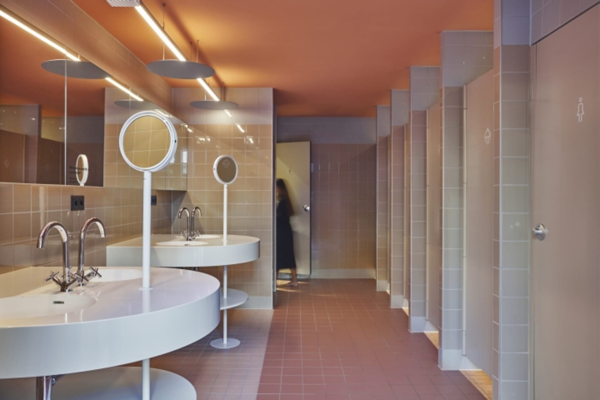 A modern public restroom with ceramic tiles, round mirrors, and sleek sinks.