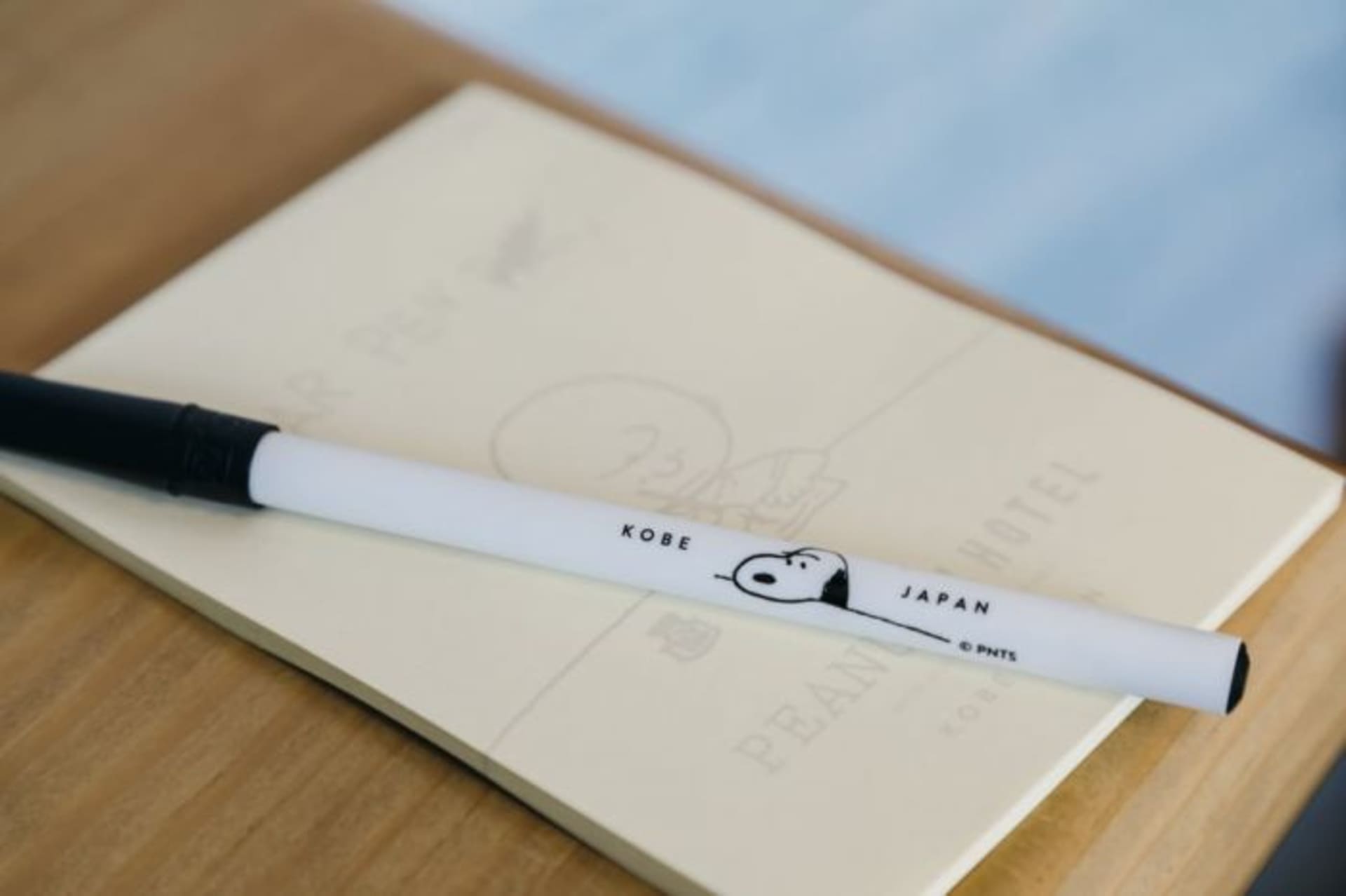 A white Snoopy-themed pen placed on a beige notepad with Japanese characters.