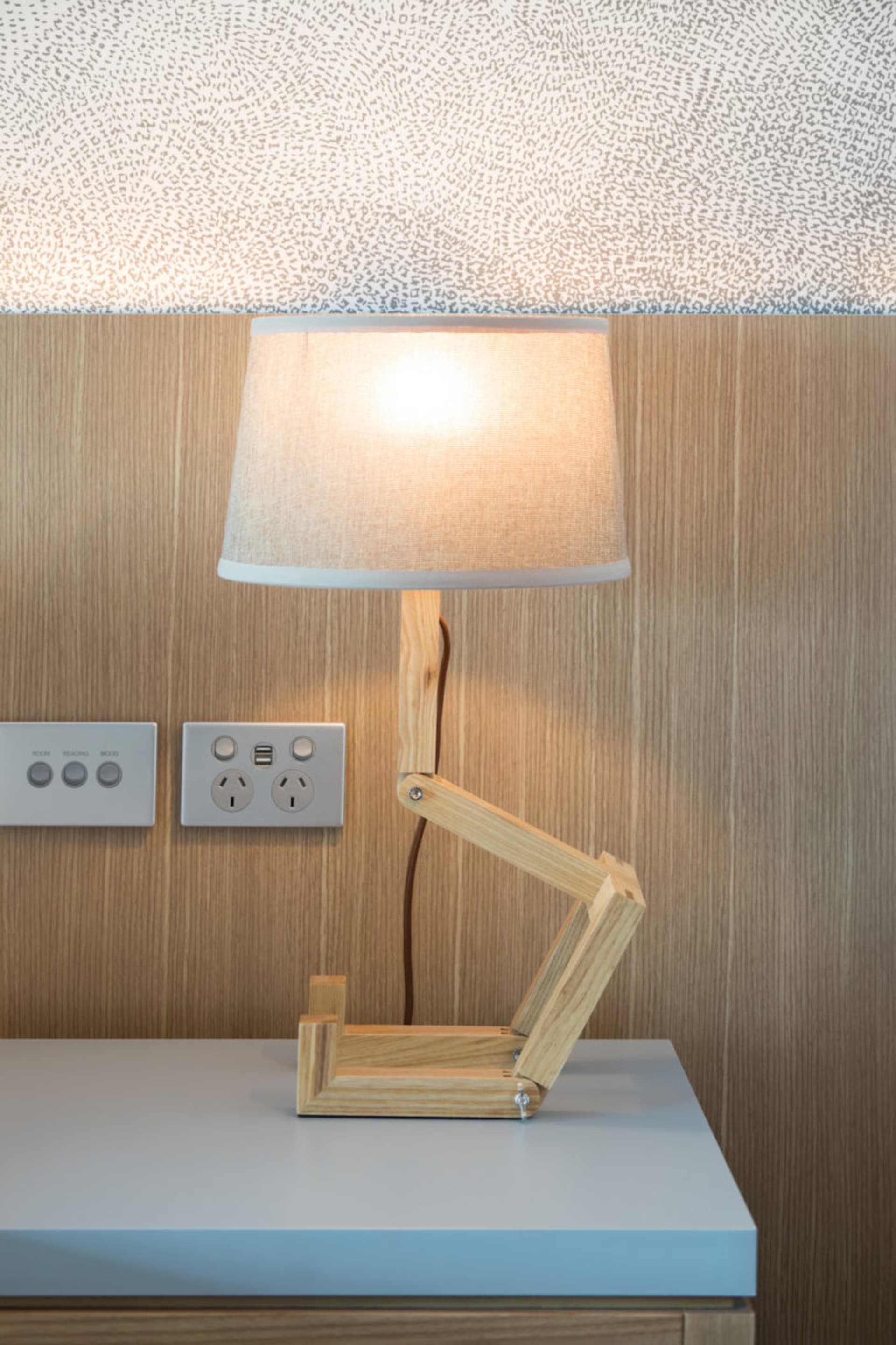 A wooden adjustable table lamp with a beige lampshade on a wooden surface.