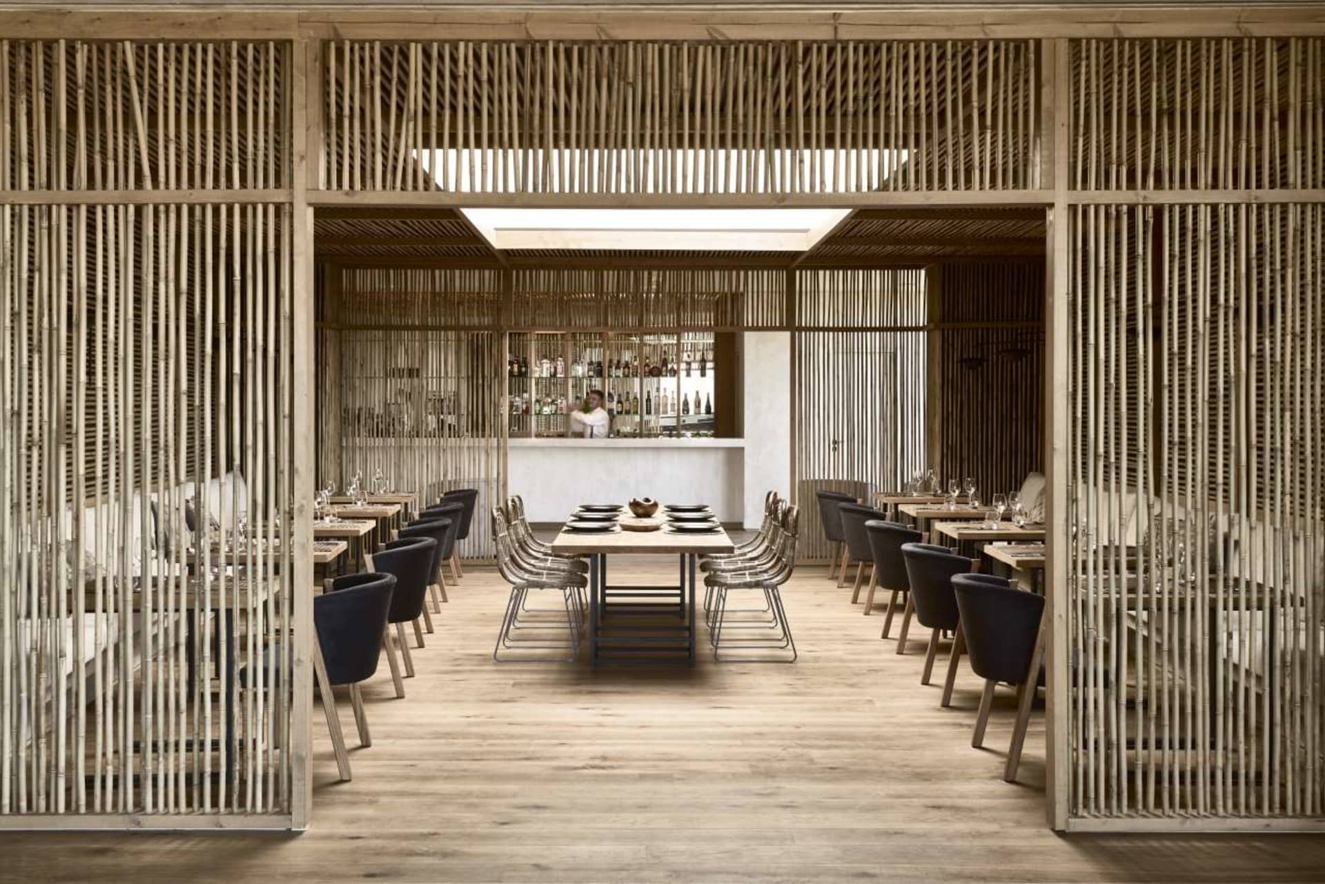 A modern restaurant with wooden interiors, featuring tables, chairs, and a bar.