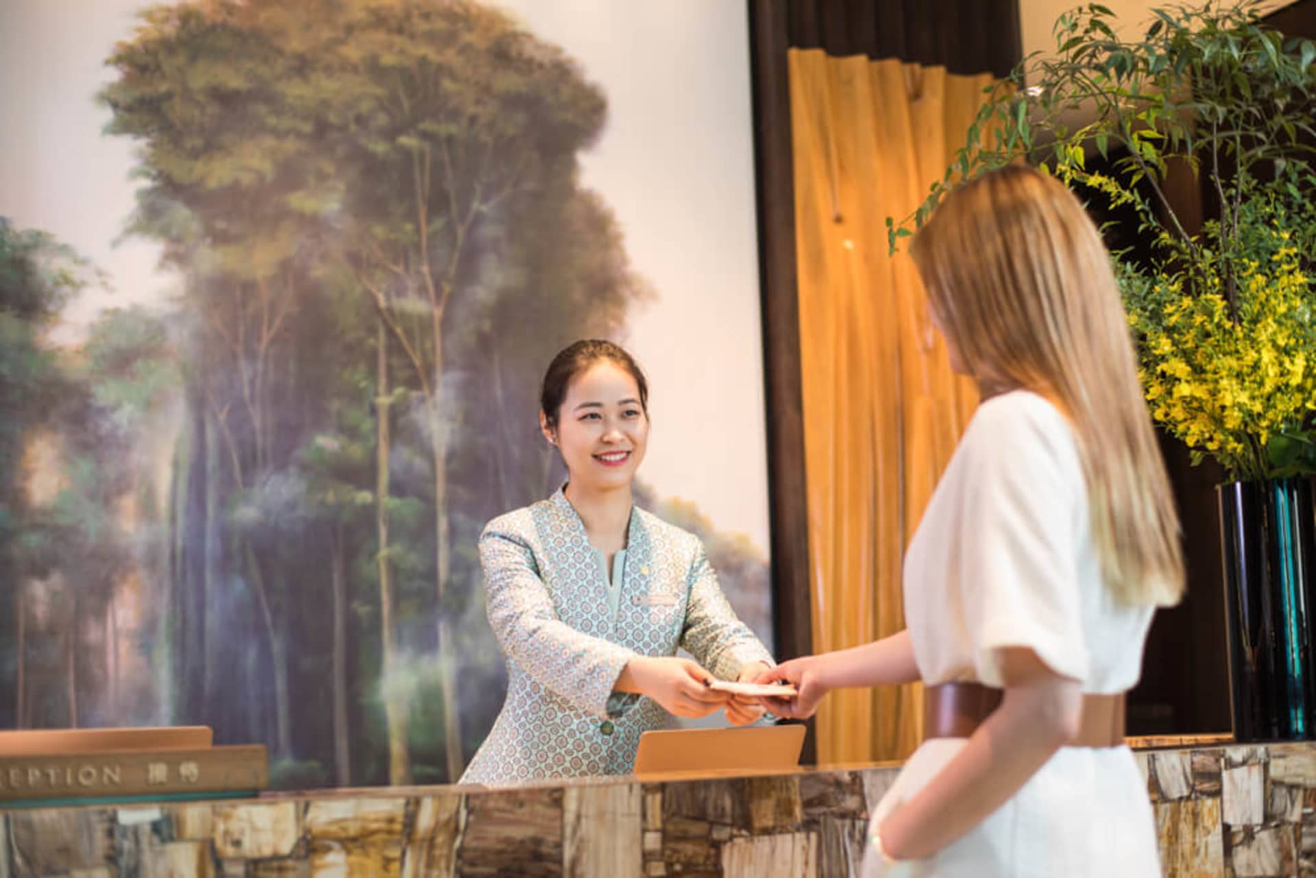 A hotel reception desk featuring a natural stone surface with a smiling receptionist interacting with a guest.