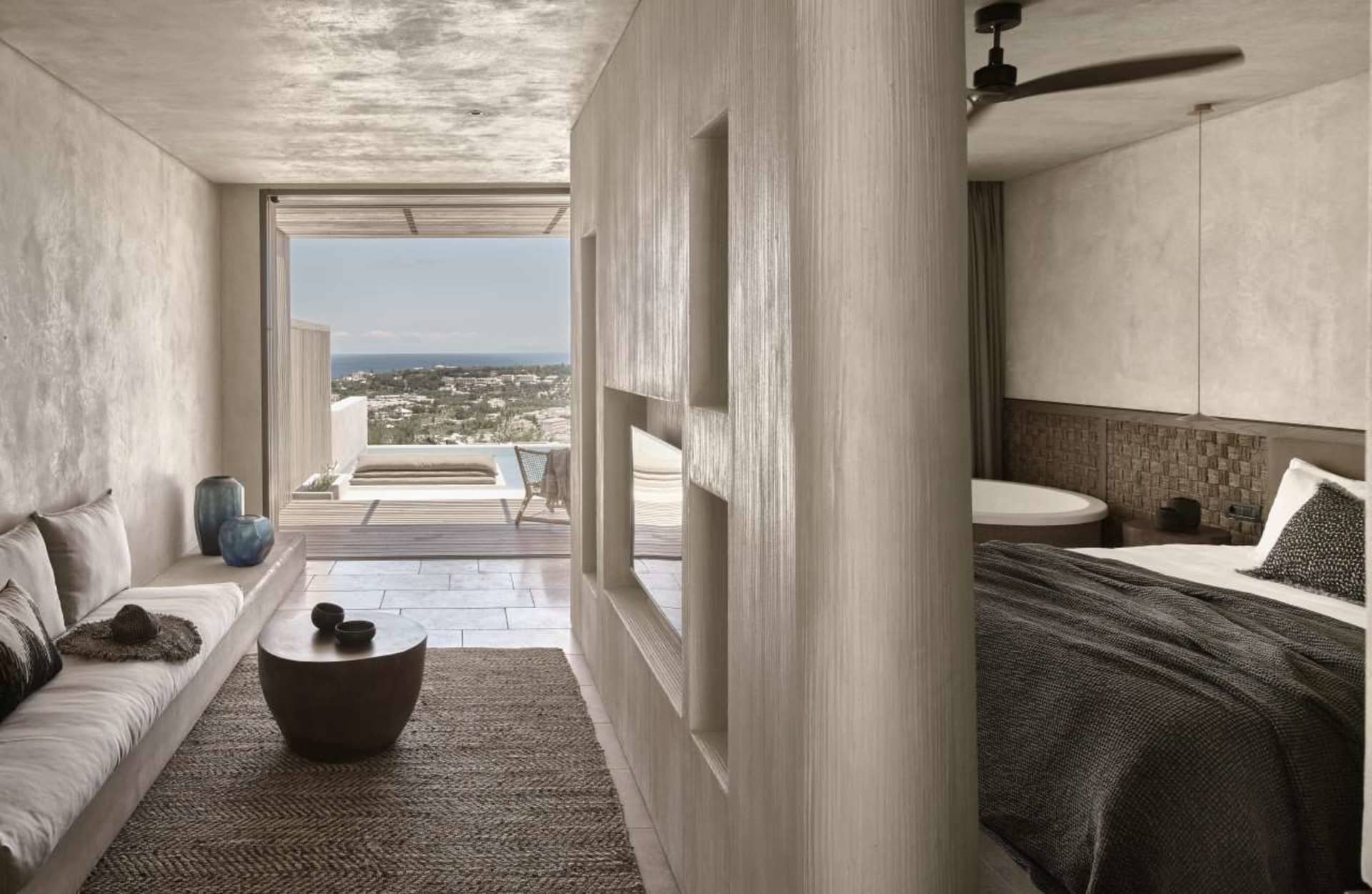 A minimalist bedroom with concrete walls, a large bed, and a view of the ocean through the windows.