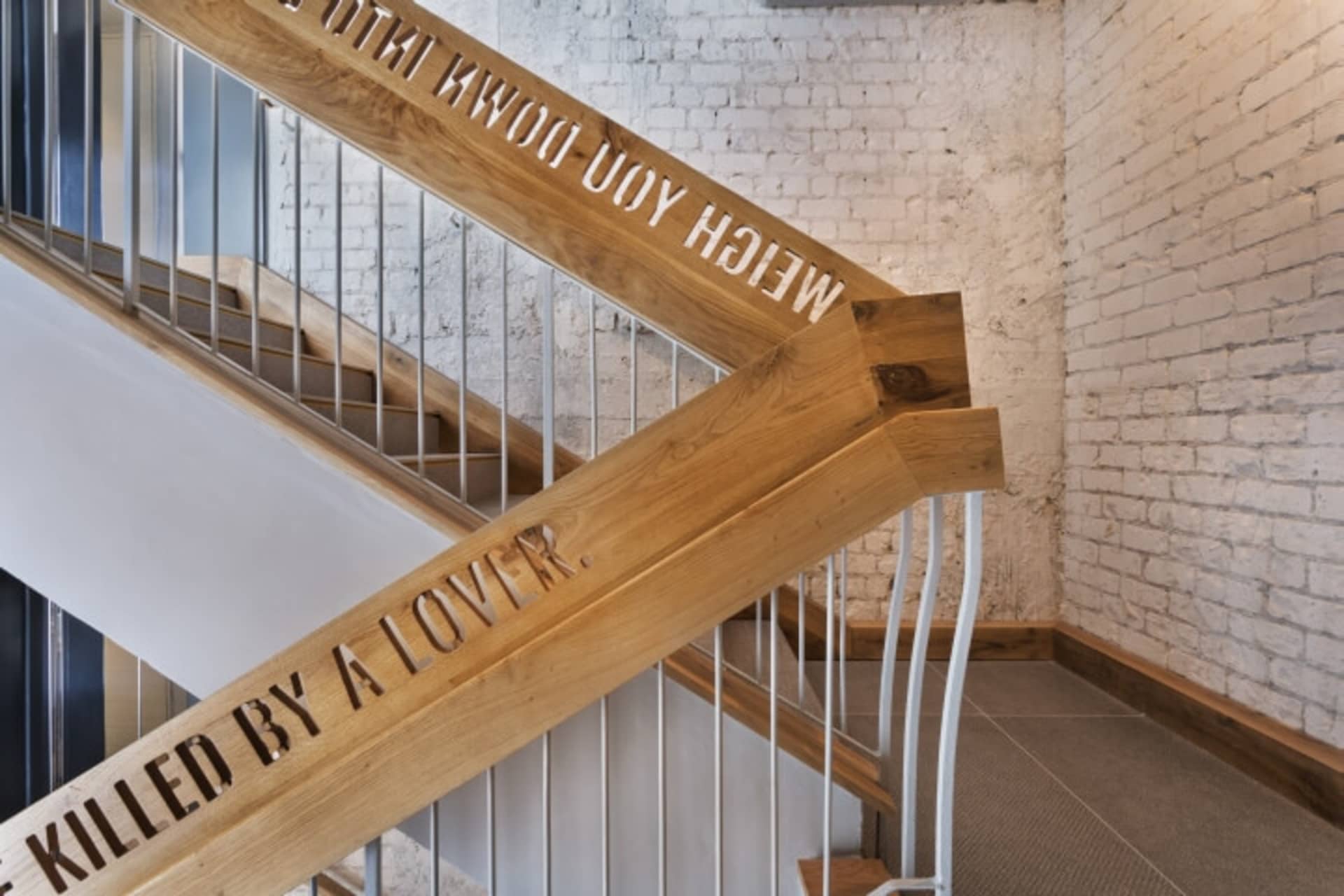 A modern industrial staircase constructed of wood with wooden brackets engraved with the phrase 'Killed by a Lover'.