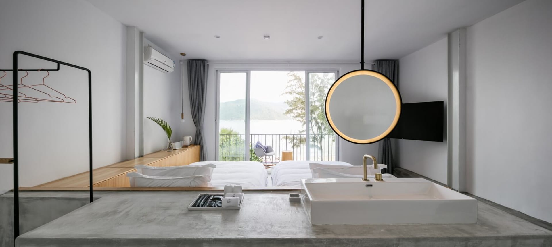 Modern minimalist hotel suite featuring a concrete floor, glass window overlooking the lake, and a circular light fixture.