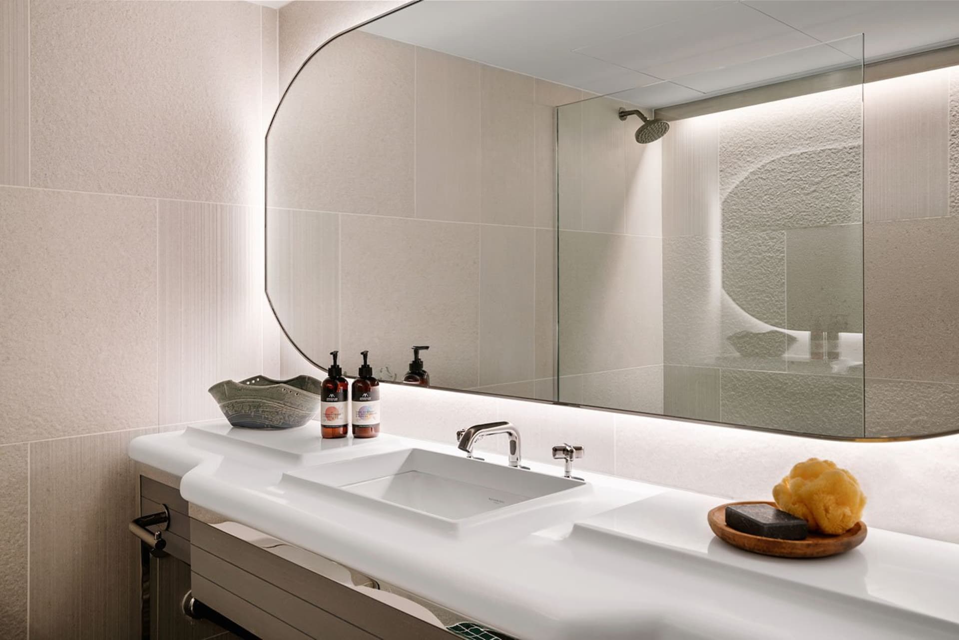 A sleek, minimalist bathroom with a white ceramic sink, glass shower enclosure, and polished surfaces.