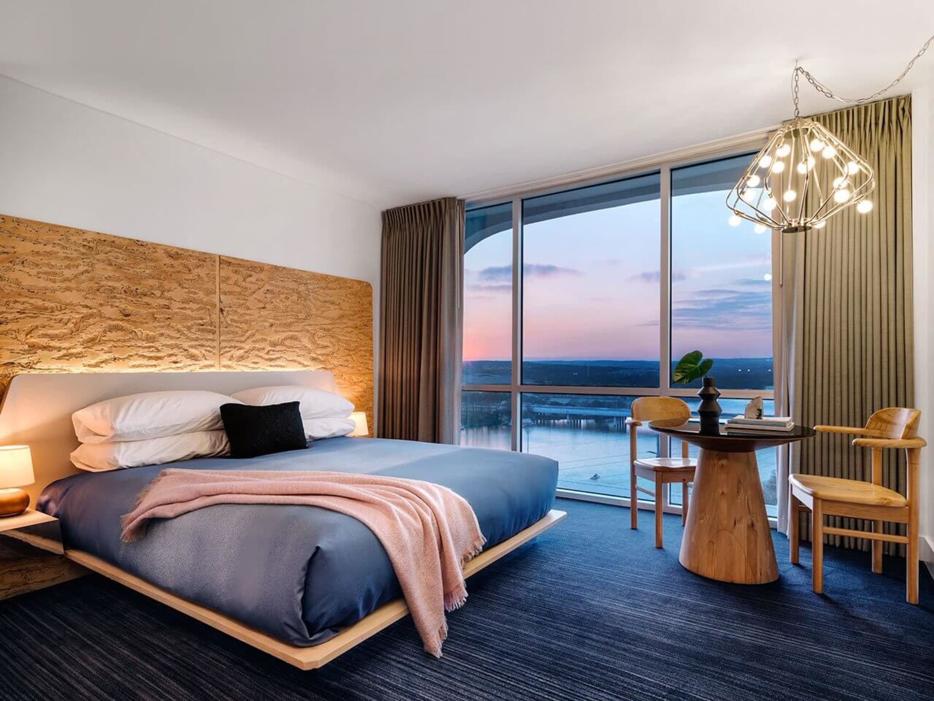 Modern bedroom featuring a wooden bed with a glass headboard, overlooking a scenic view through large windows.