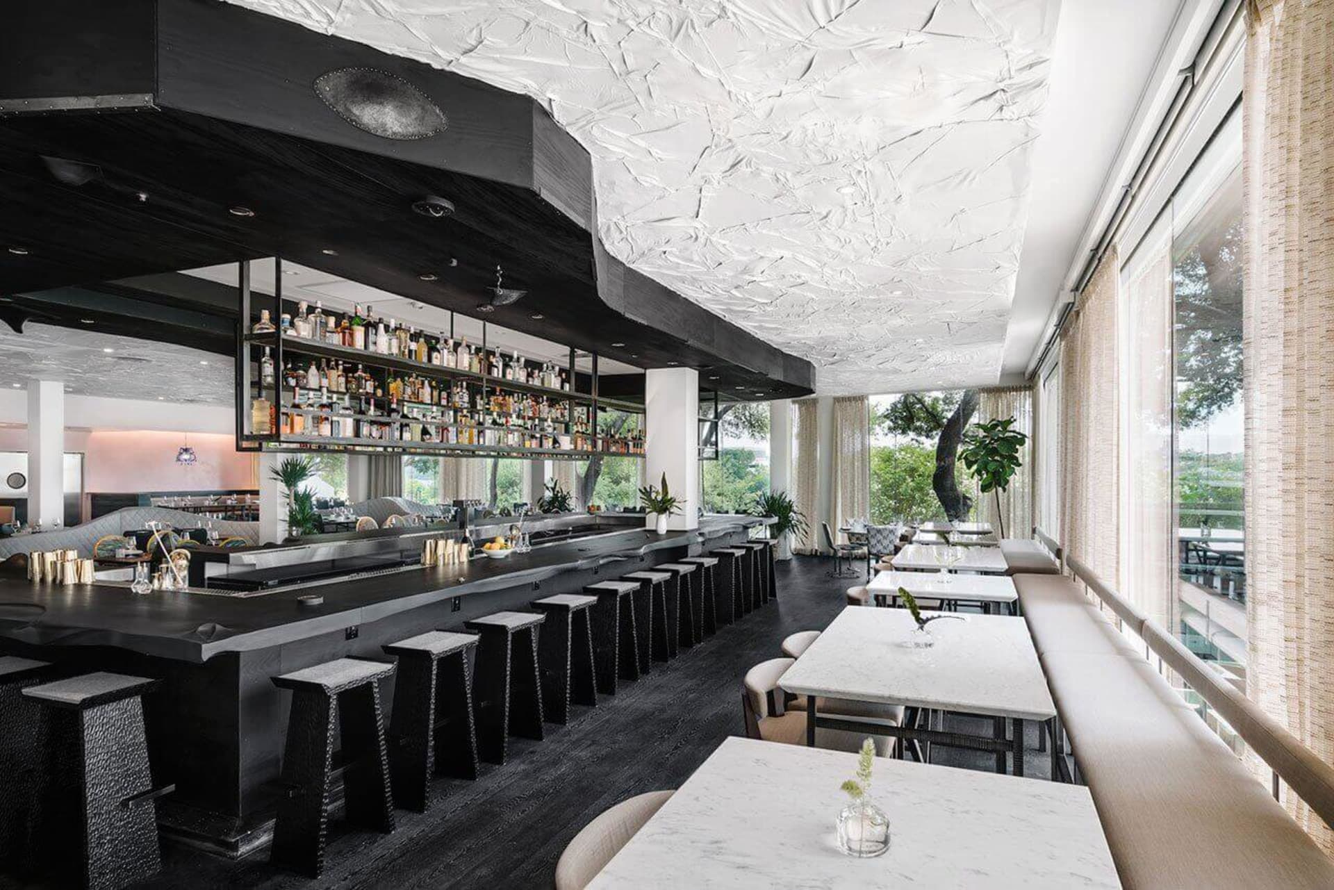 Modern cafe bar with white concrete precast walls and ceiling, featuring a well-lit bar area with stools and a long table for
