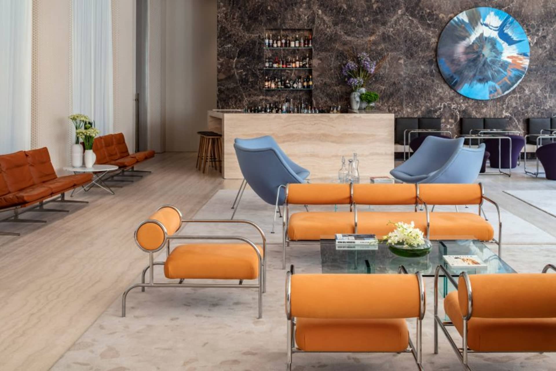 Modern hotel lobby featuring orange leather seating, marble accents, and metal framework.