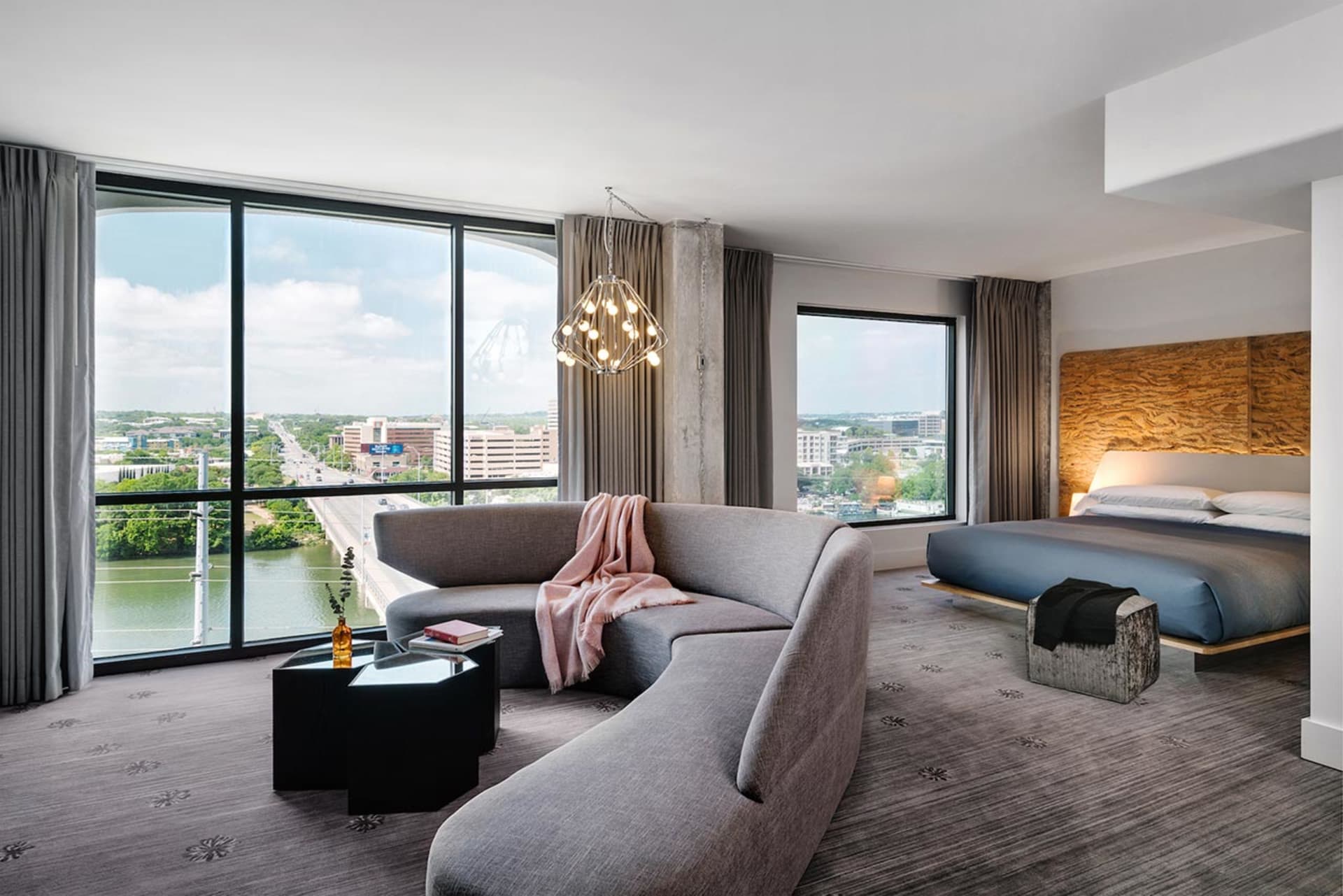 Modern hotel room featuring a contemporary couch, bed, and large window overlooking a cityscape.