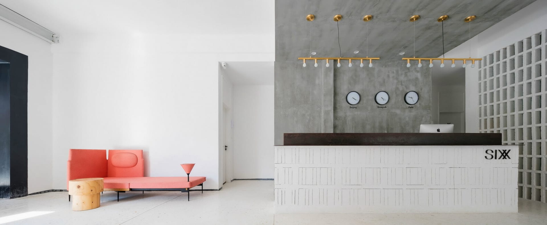A modern lobby featuring a reception desk with clocks displaying time zones and a minimalist seating area with a pink couch a