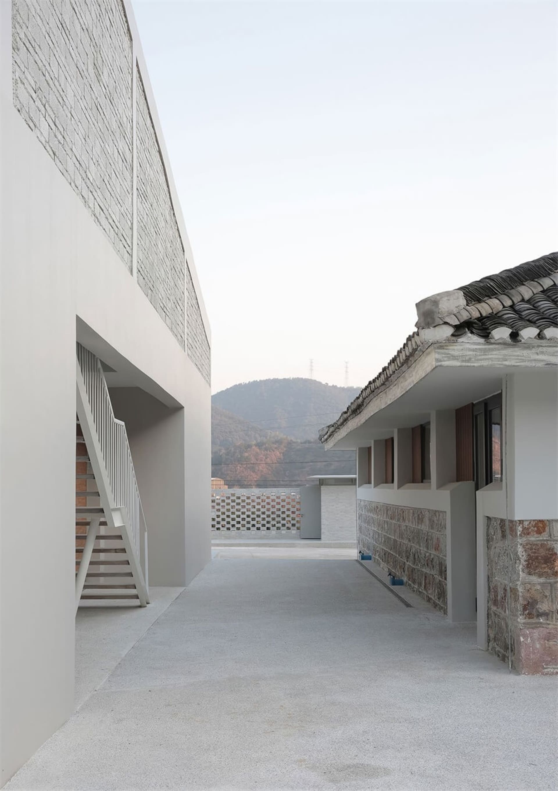 Modern residential building with a concrete exterior and white walls, featuring a stone staircase and a tiled roof.