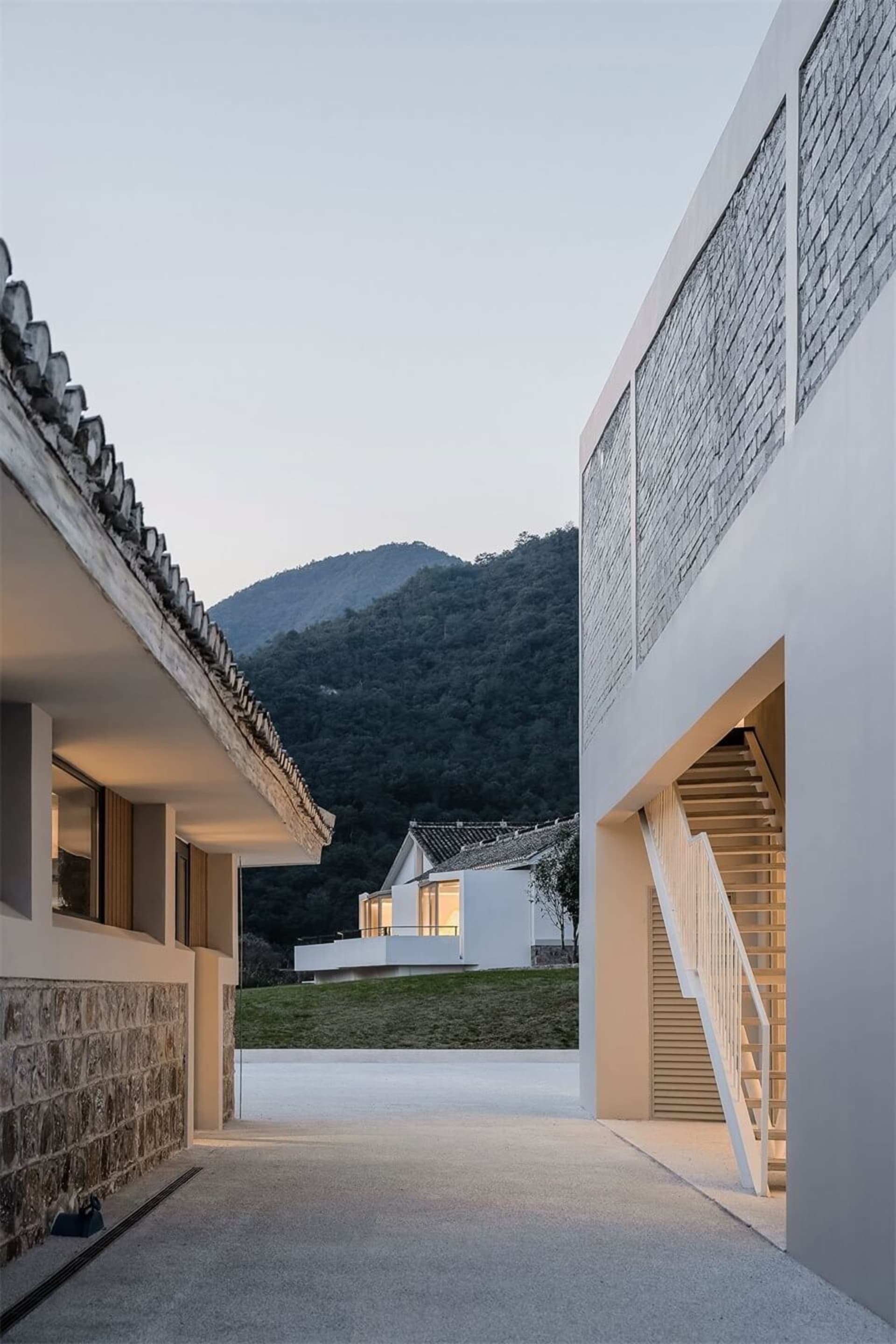 Modern residential exterior featuring concrete and wood materials, with a mountainous background.