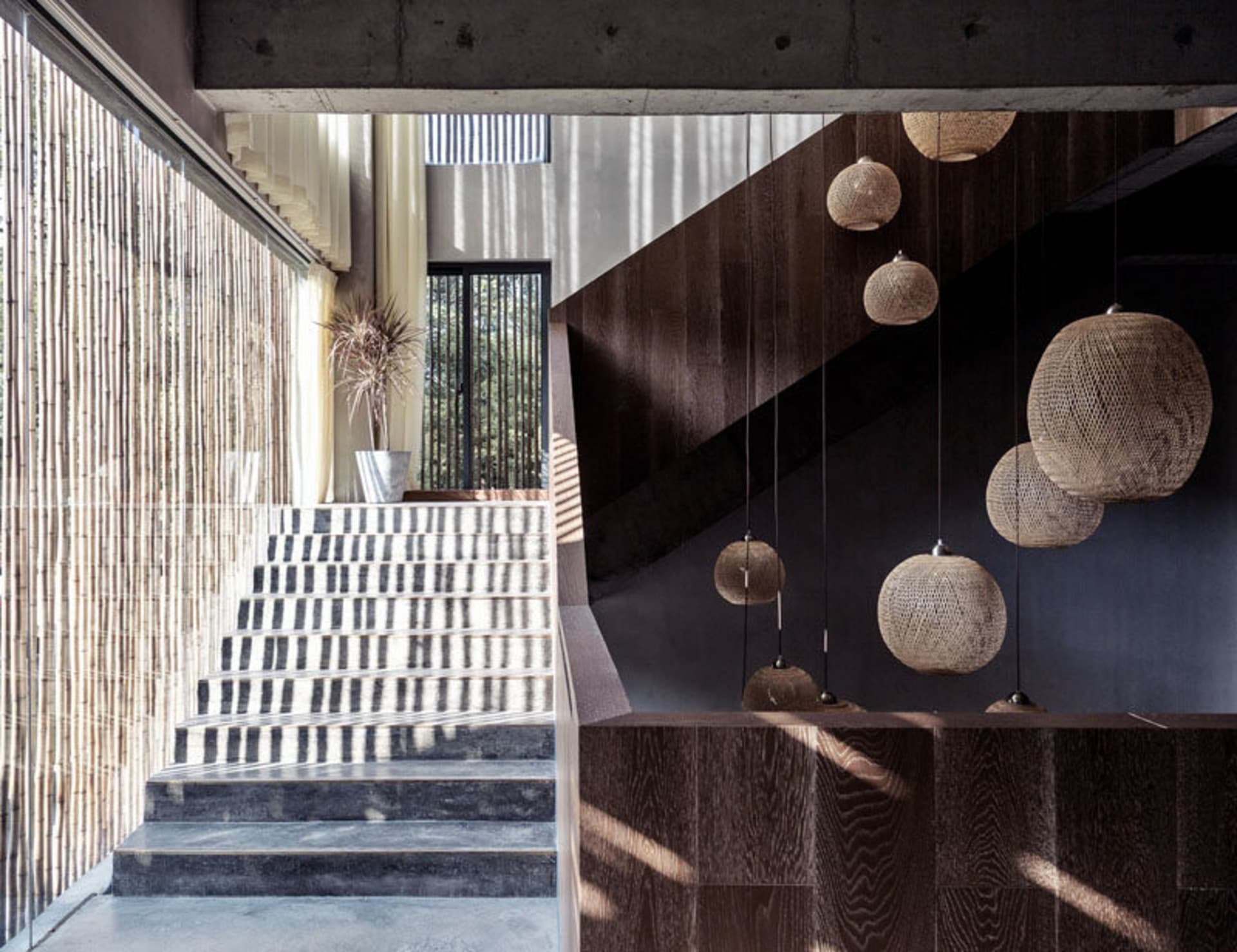 A modern staircase with wooden stairs, concrete walls, and bamboo lighting fixtures.