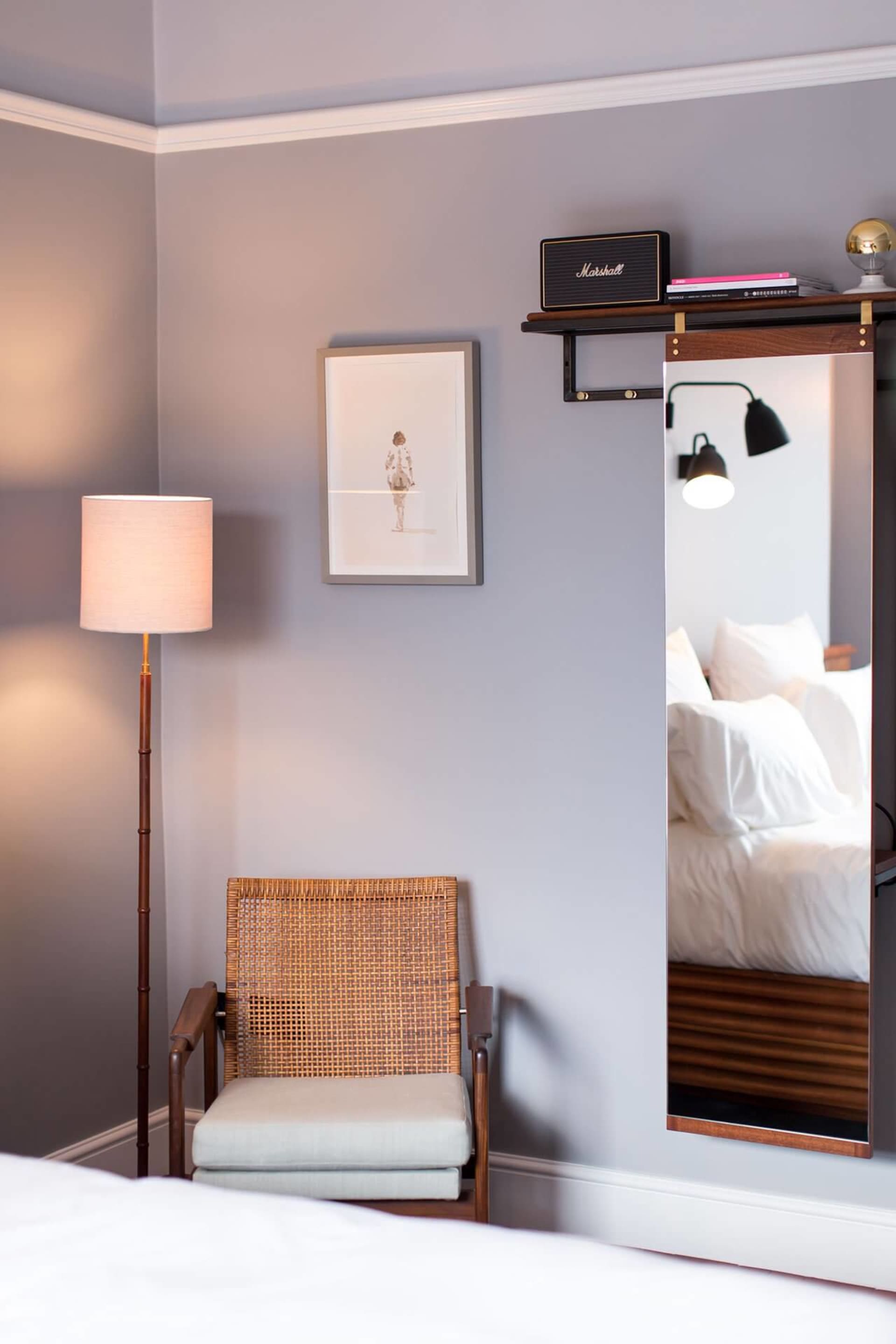 A modern bedroom featuring wooden and rattan furniture with a cotton-covered chair and a tall lamp with a white shade.
