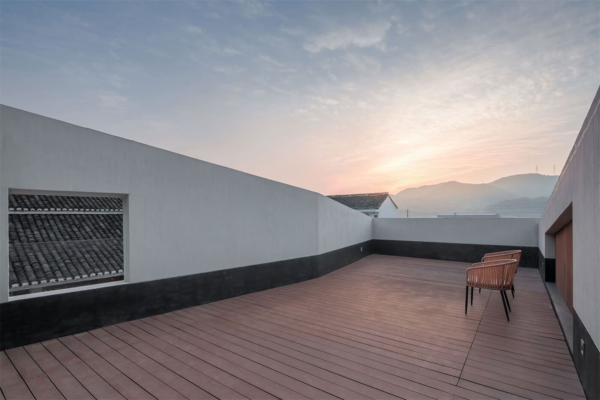 Modern rooftop terrace with wooden tiles and a view of distant mountains and sunset.