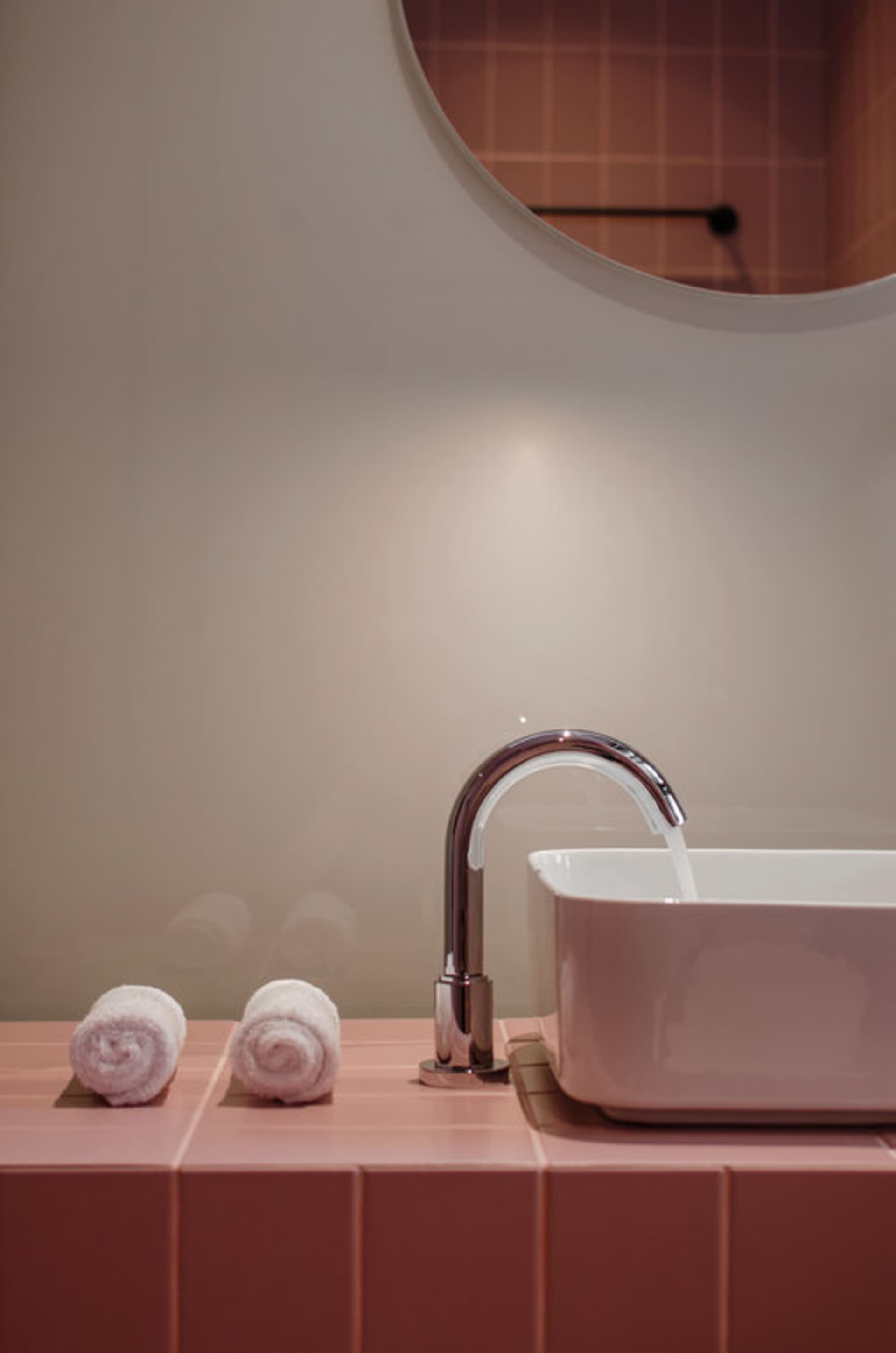 Modern bathroom with a sink, faucet, and three white towels on a pink tiled countertop.