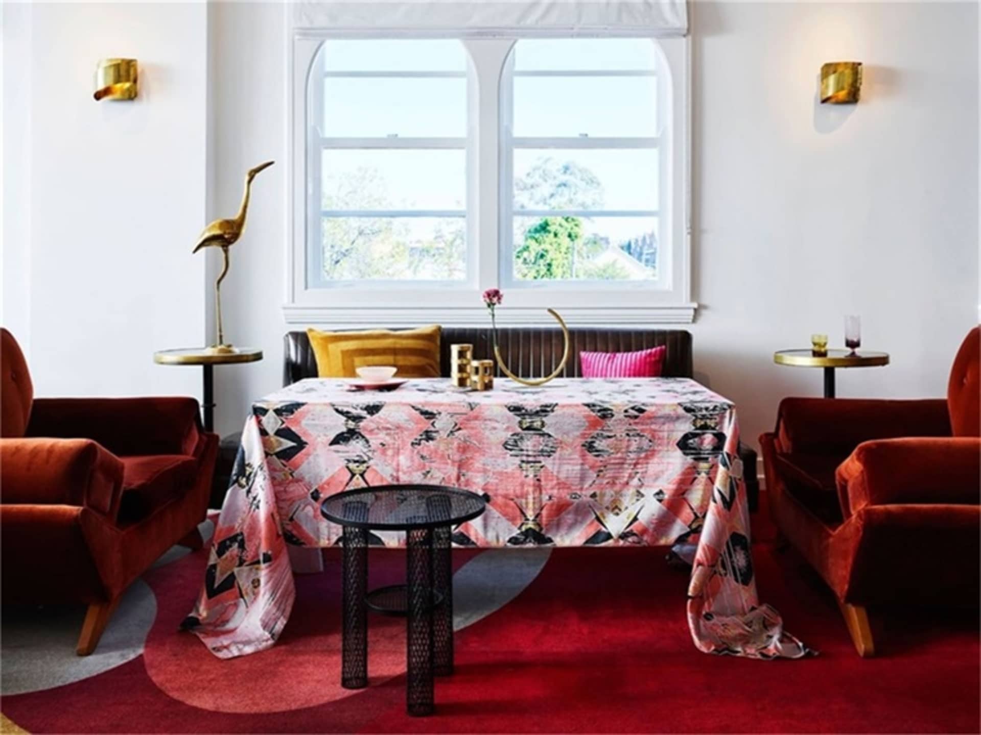 A contemporary living room featuring a patterned textile tablecloth, red velvet chairs, and brass accents.