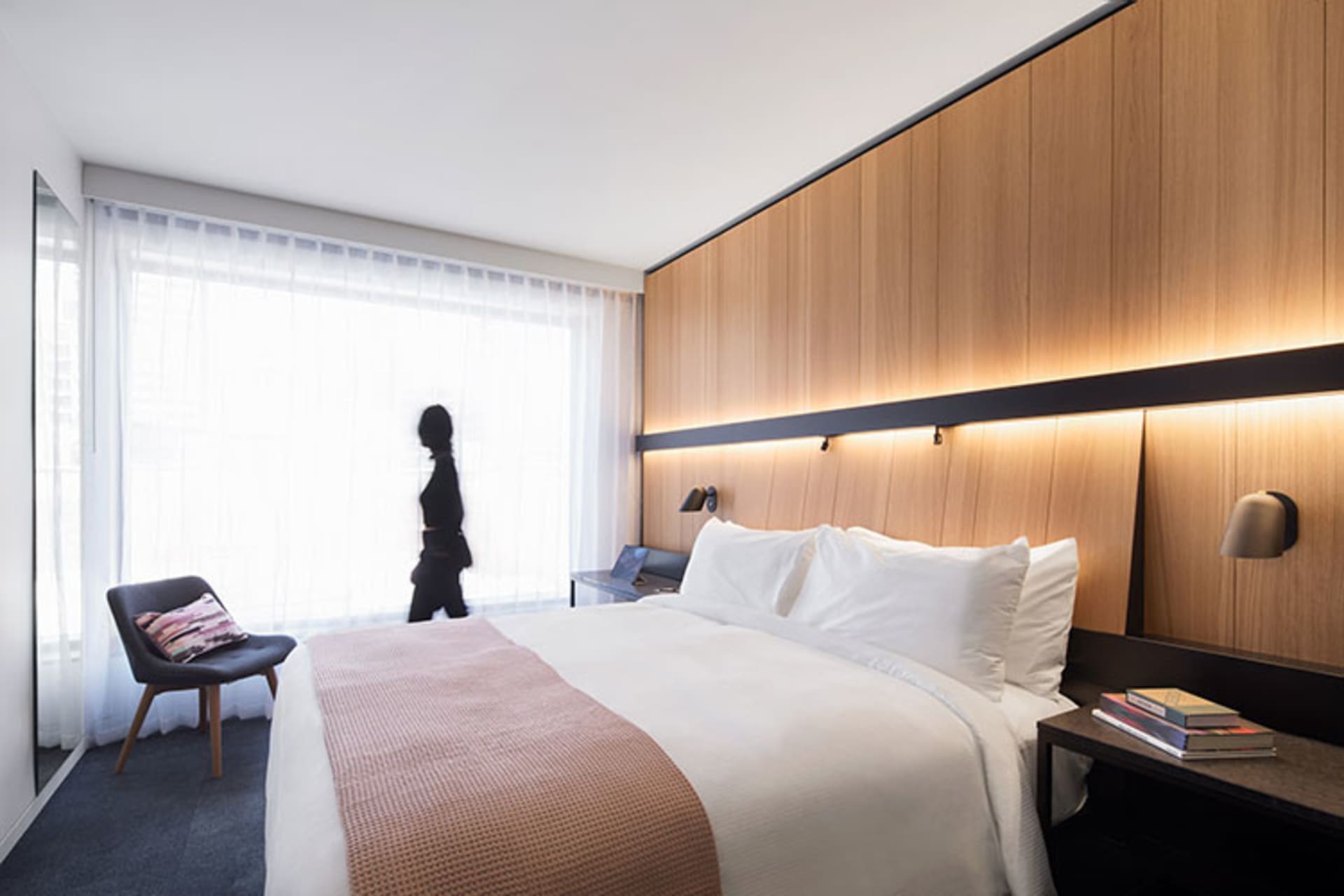 簡約臥室內設有一張大型床鋪，搭配木質床頭板、白床單，以及一張置有兩本書與檯燈的床邊桌。