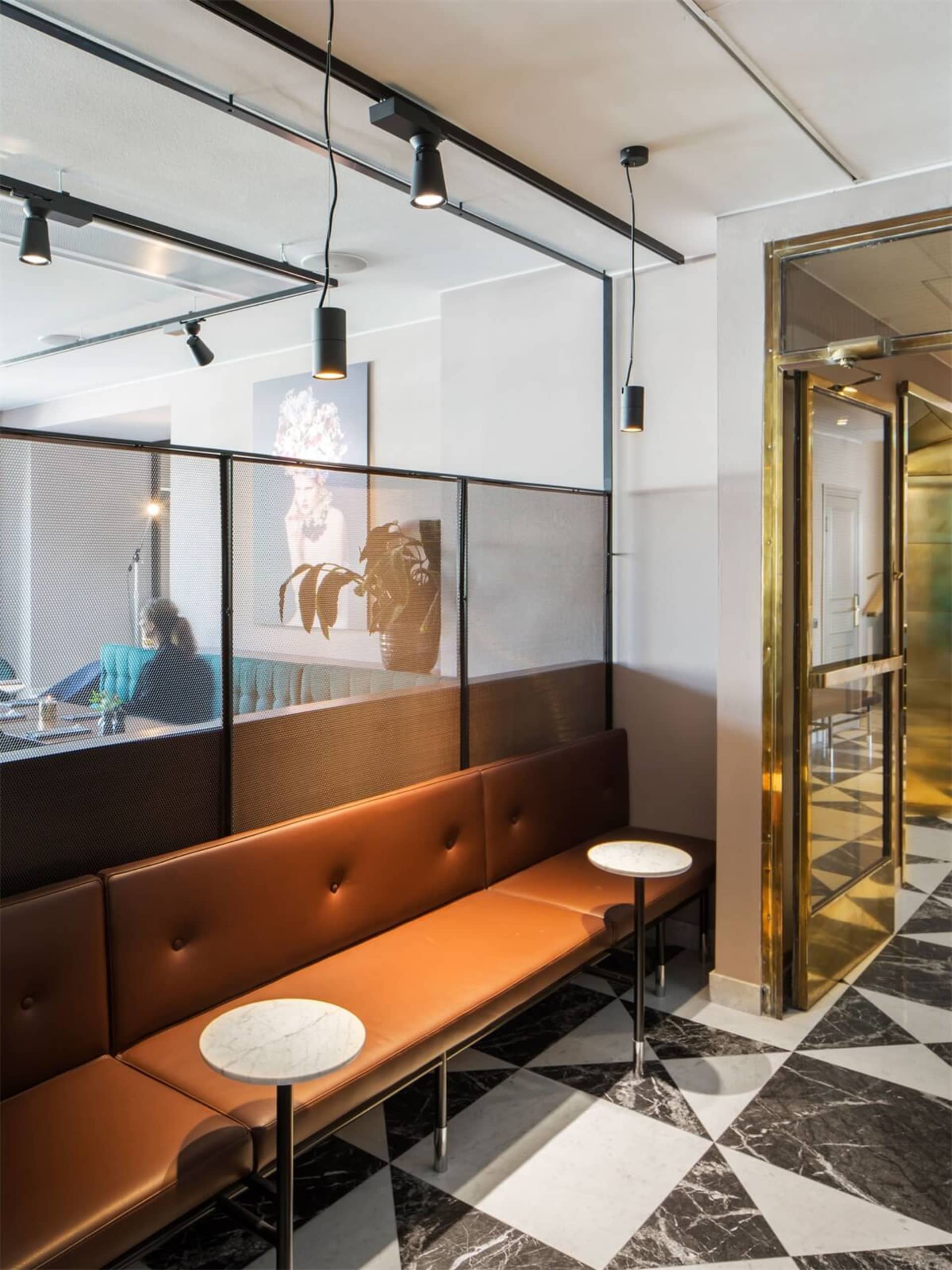 A minimalist restaurant interior featuring a leather bench, marble floor, and metal railings.