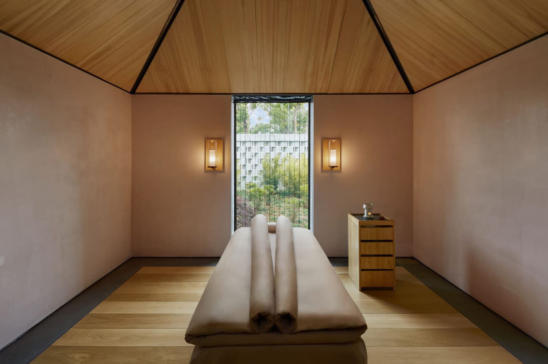 A serene spa massage room featuring wooden elements and a view of nature through a window.