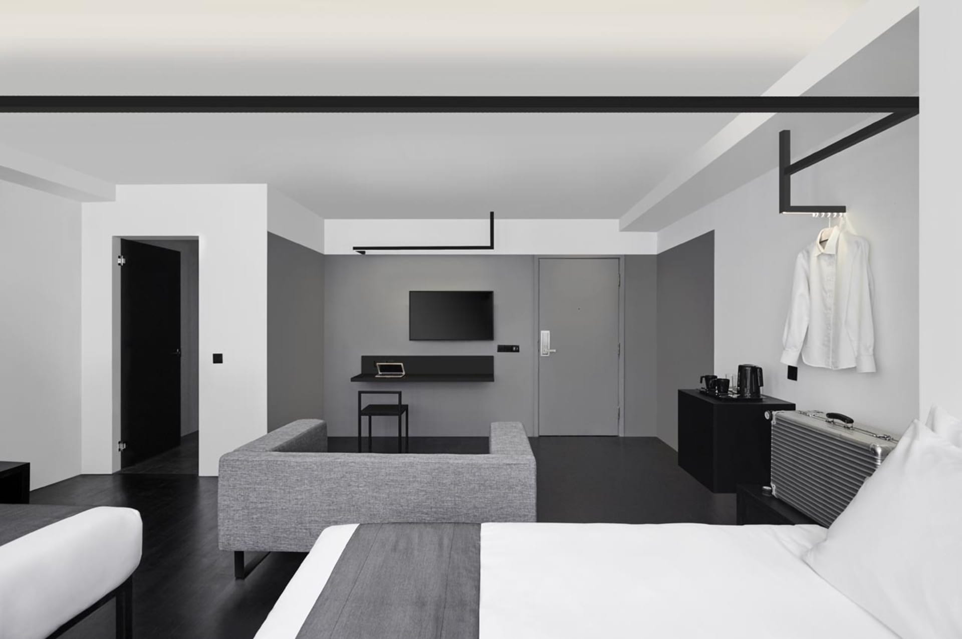 Modern minimalist hotel room featuring a concrete floor and furniture, with a television mounted on the wall and a stylish wh