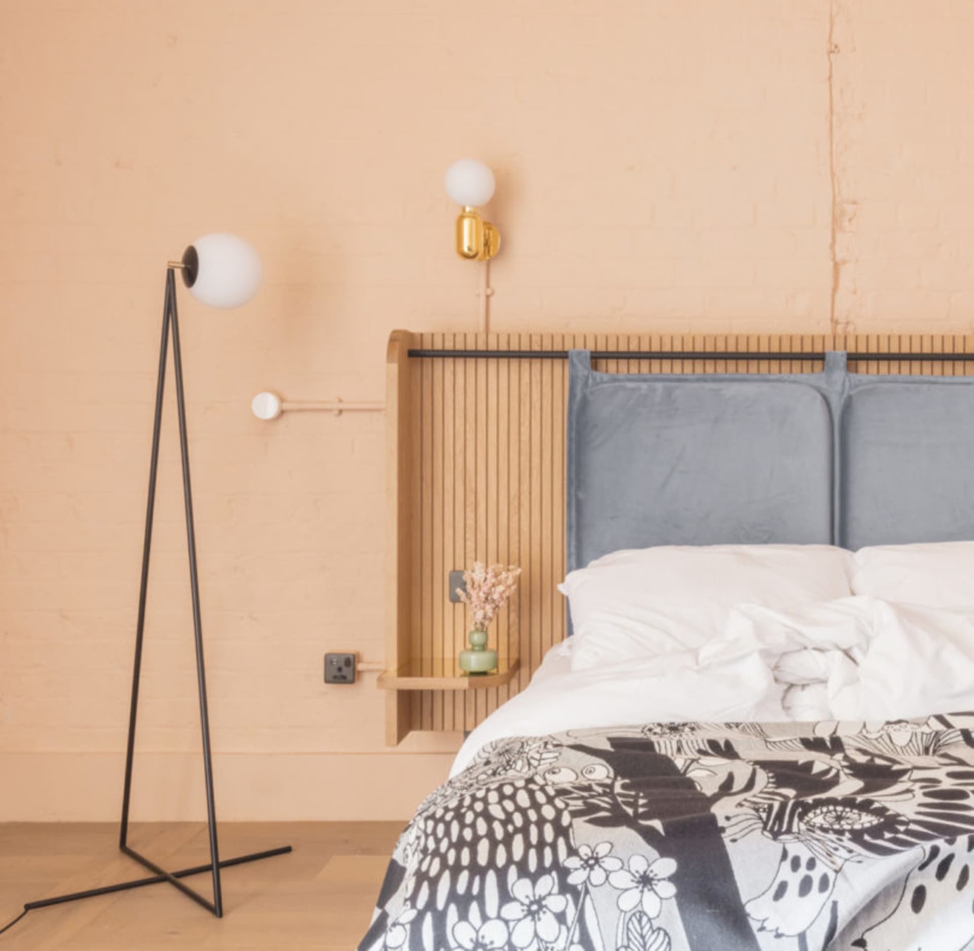A modern minimalist bedroom featuring a wood headboard, a grey upholstered bed, and a white floor lamp with a round white glo