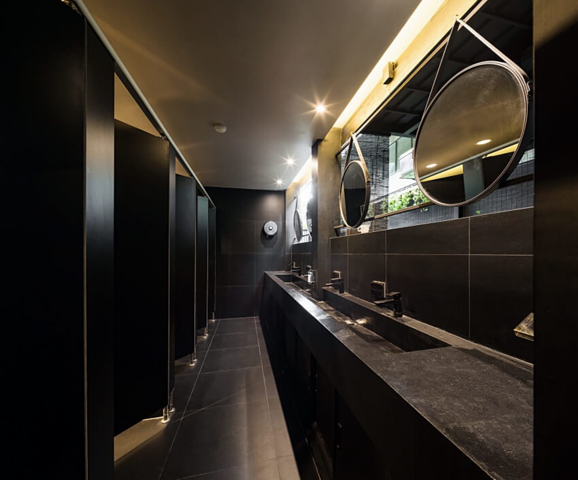 Modern black-tiled restroom with metal finishes and round mirrors.