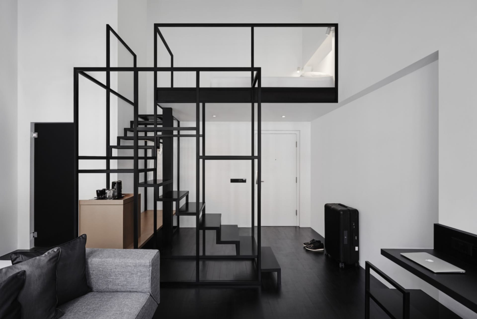 A minimalist living space with a metal staircase and metal walls, featuring a grey couch, a desk, and a loft bed.
