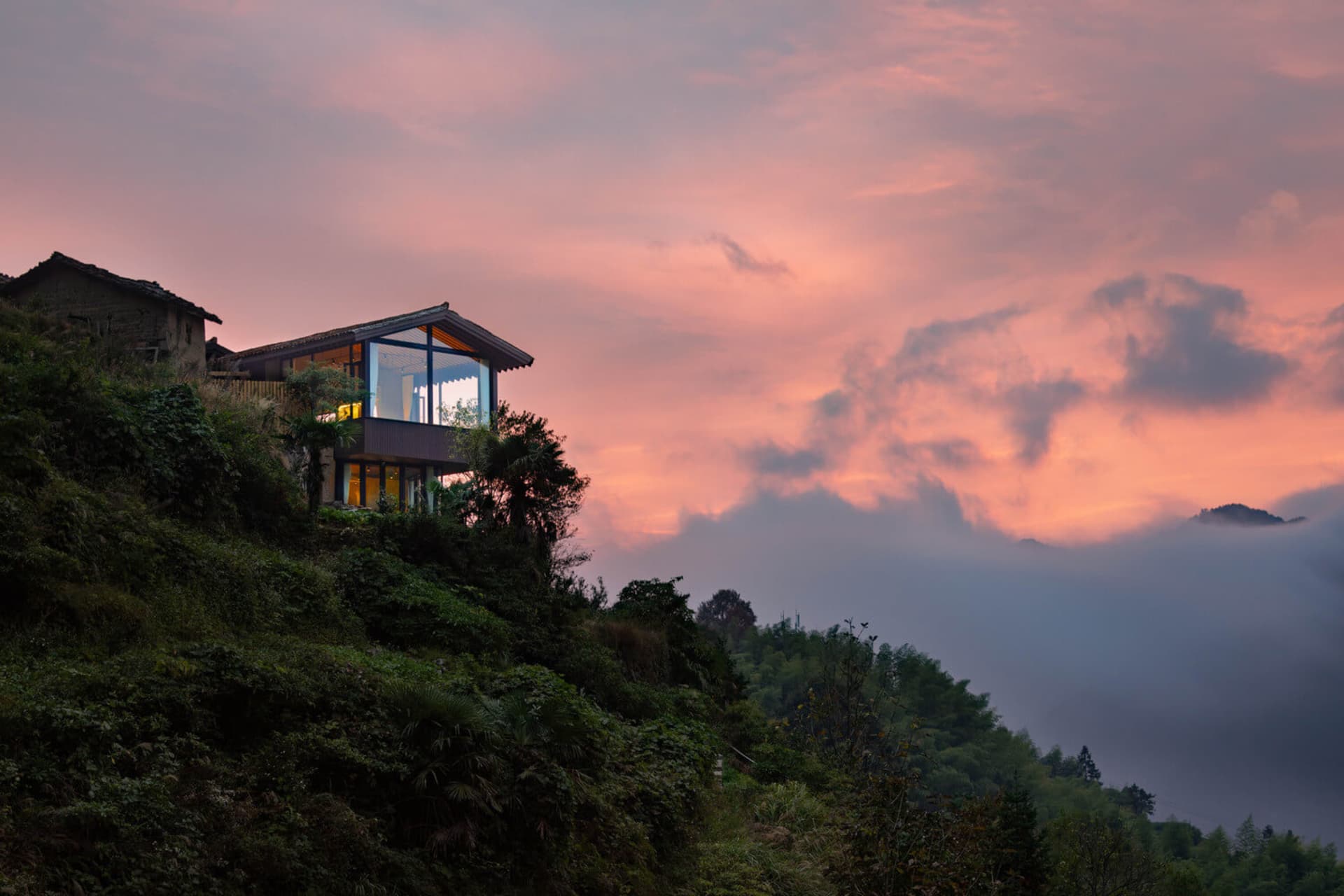 現代住宅擁有玻璃牆面與鋼構結構,坐落於山坡上,夕陽餘暉映照。