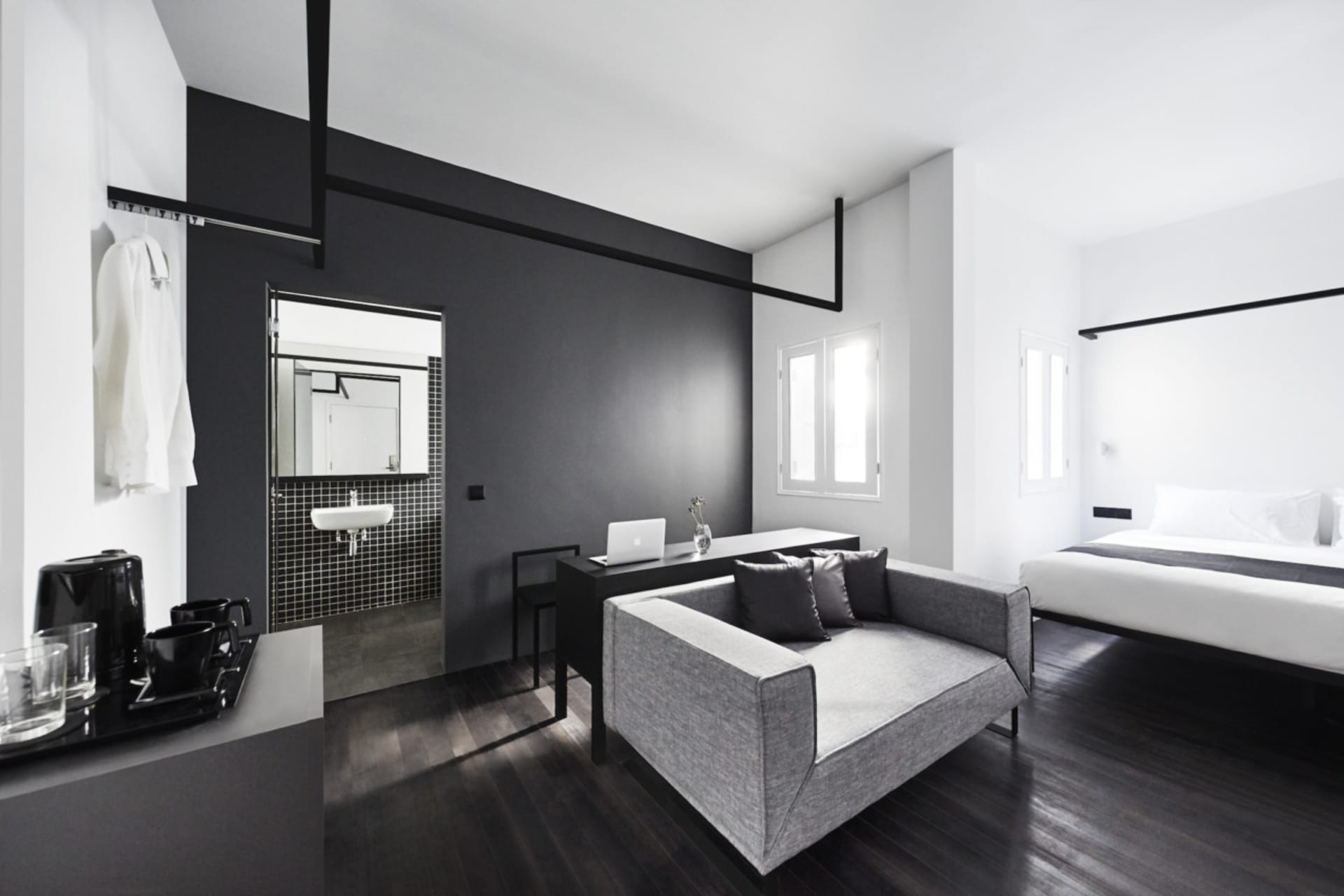 A modern minimalist bedroom with black, white, and gray tones featuring a simple sofa, a bed with a black and white comforter
