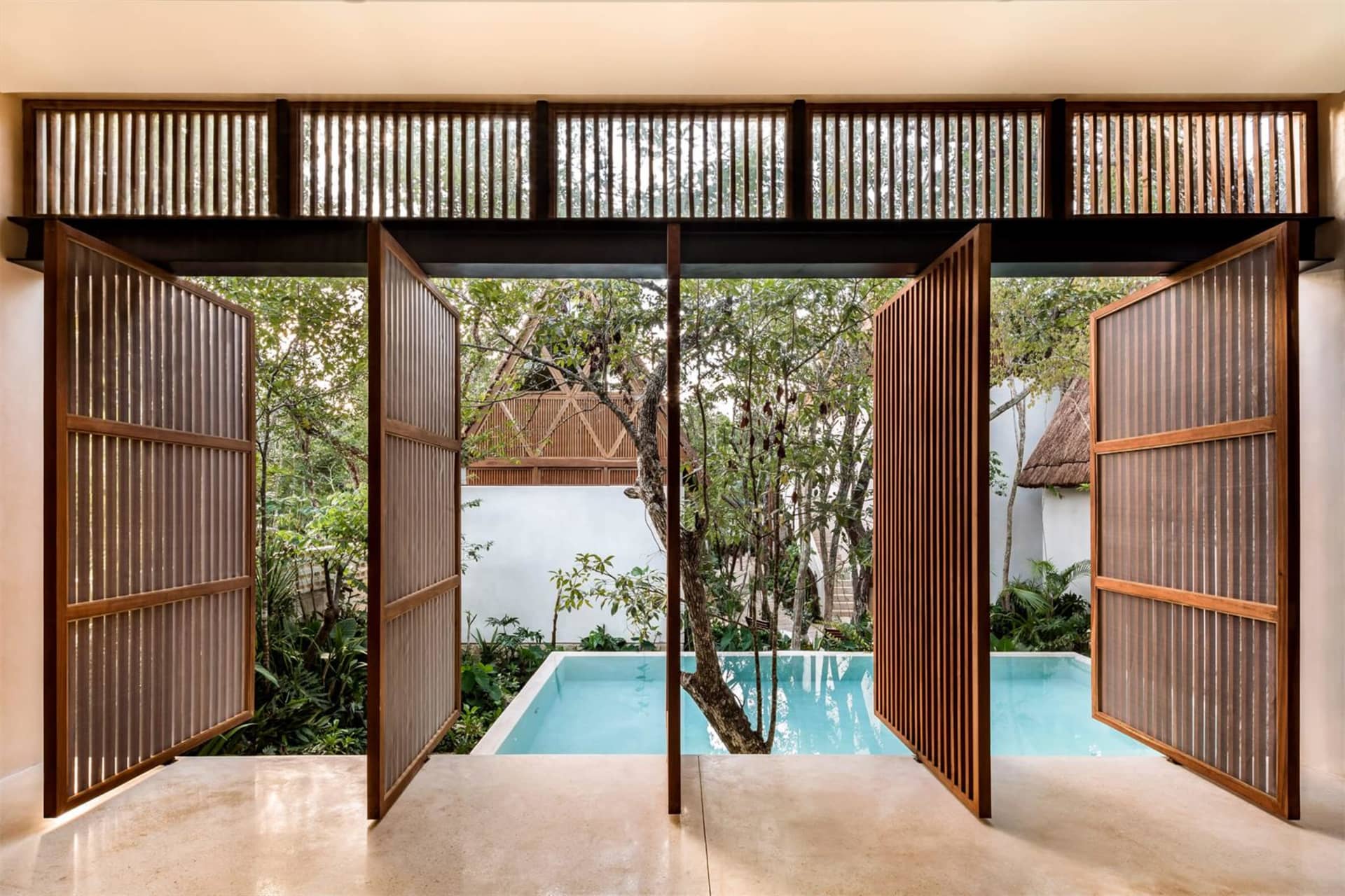 An open wooden gate, revealing a serene pool and lush greenery.
