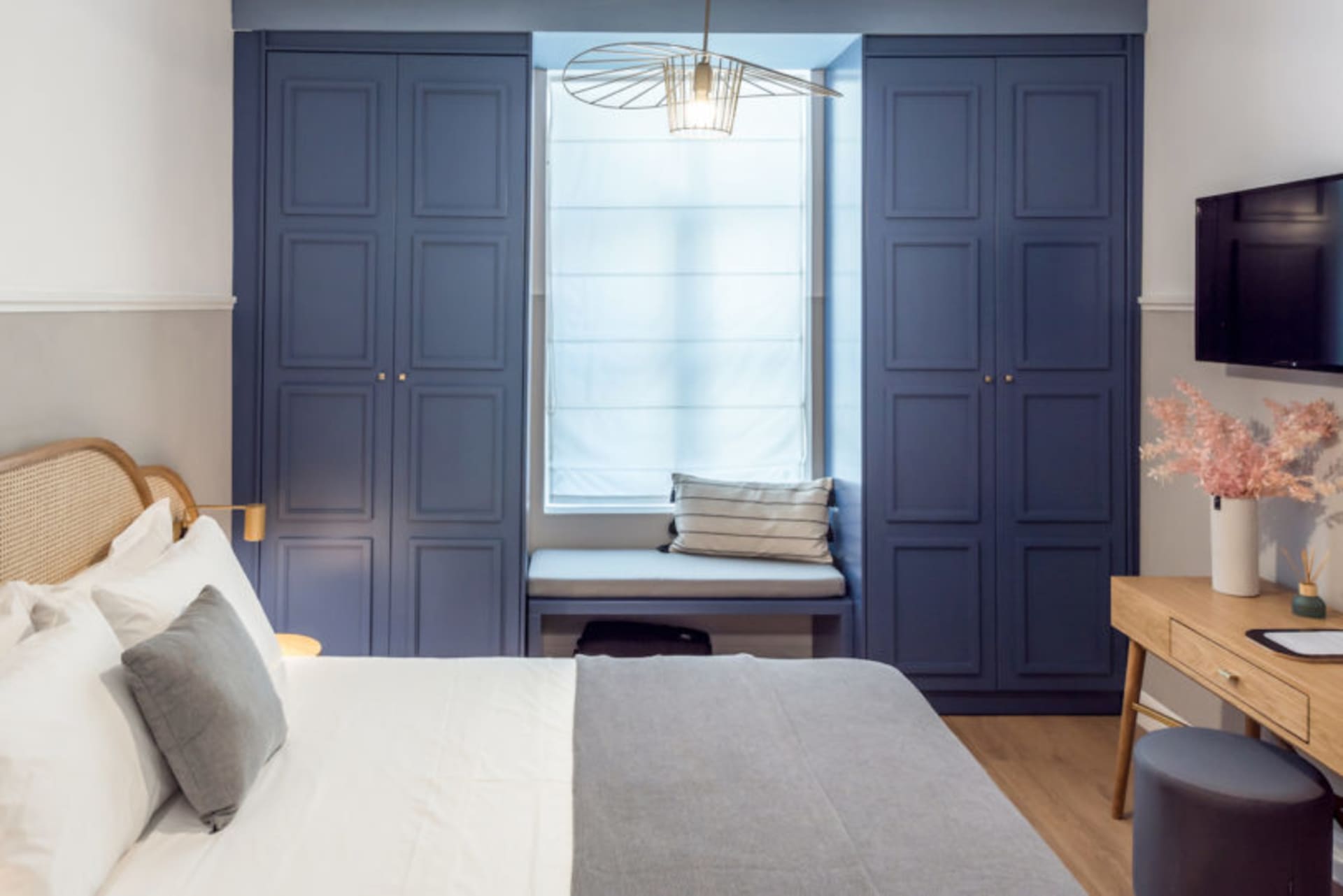 A modern bedroom featuring wooden furniture with a white bed, blue cabinets, and a bench seat by the window.