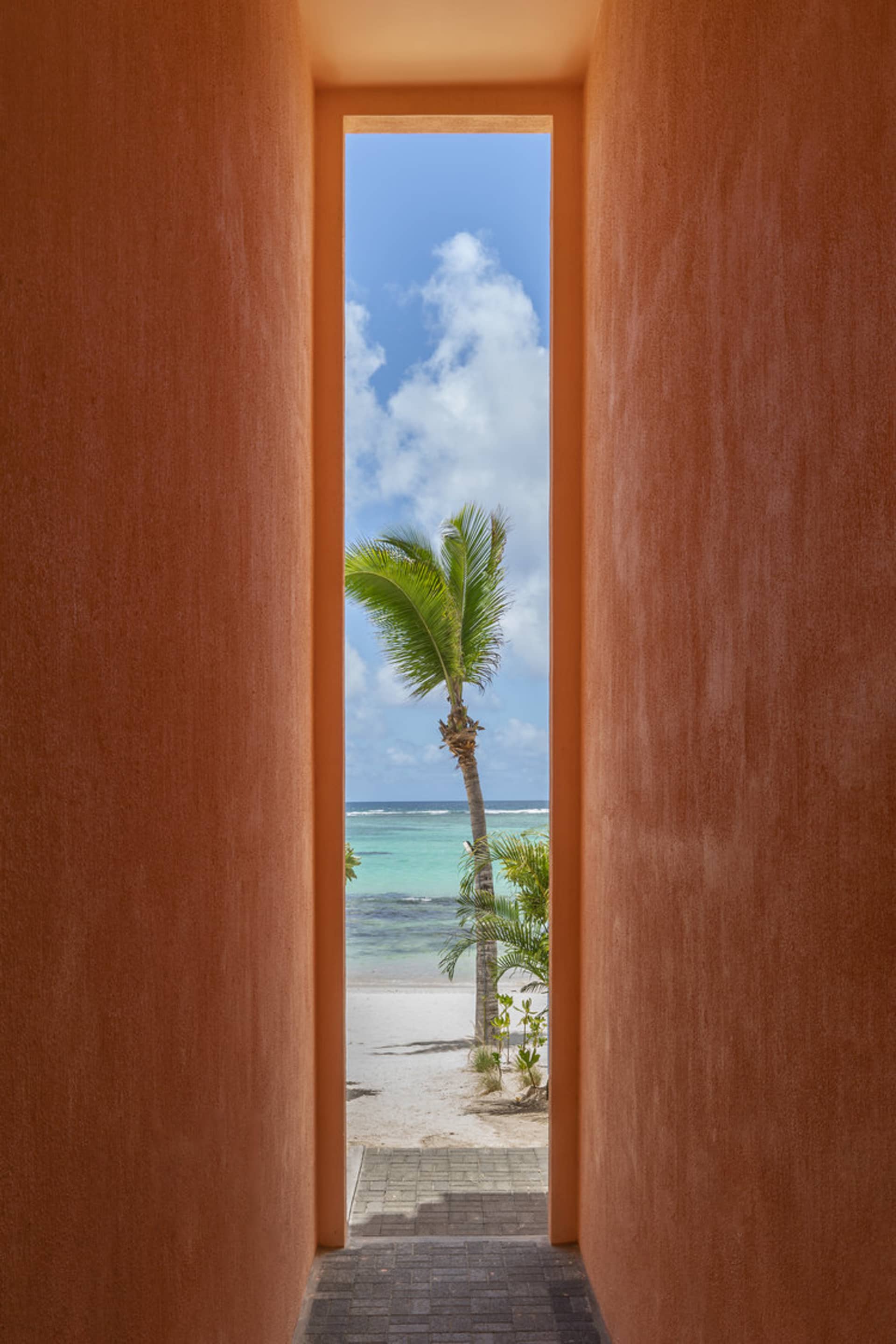 A view through a red doorway showing a palm tree and sandy beach.